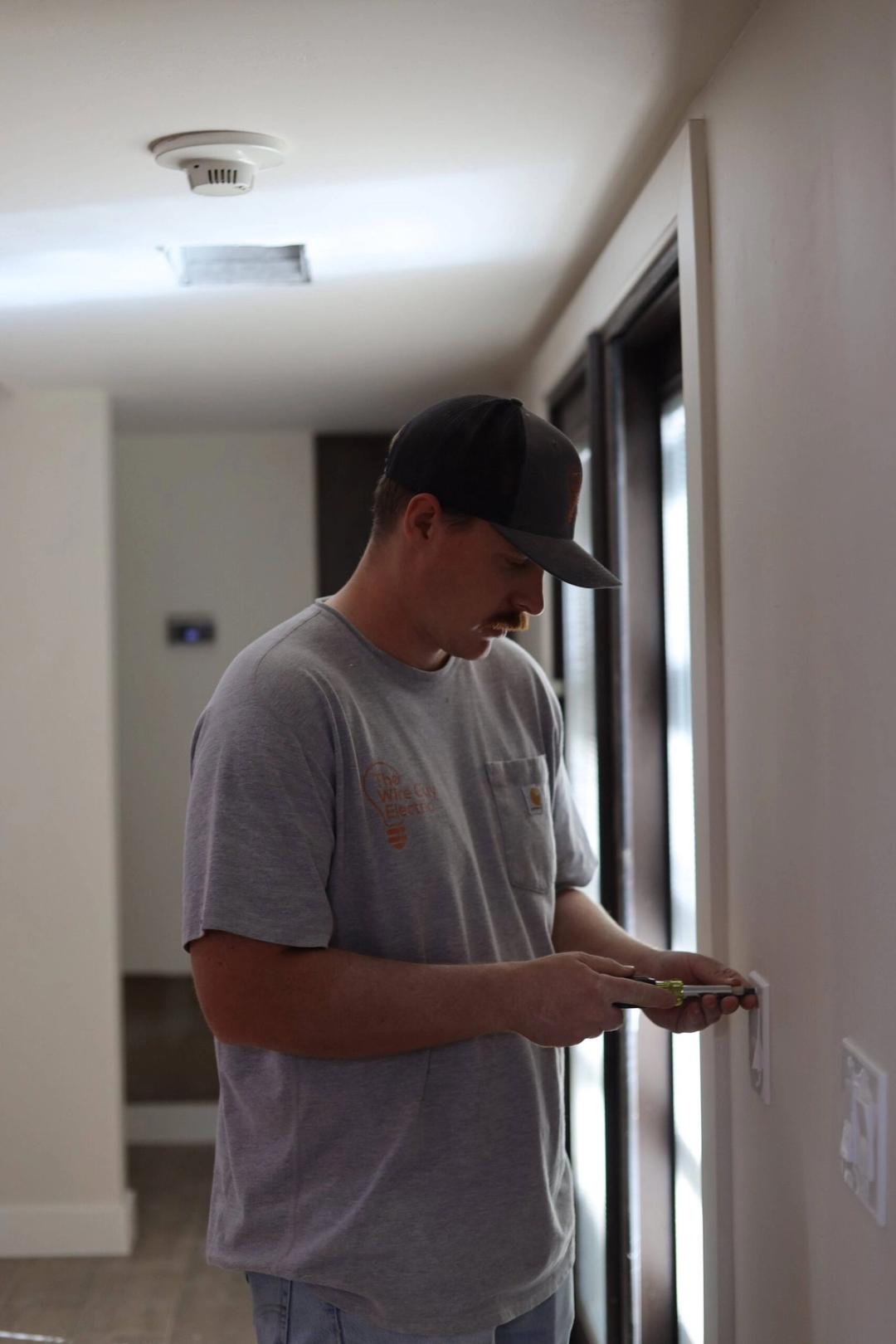 Electrician testing a wall receptacle with a tester in a hallway