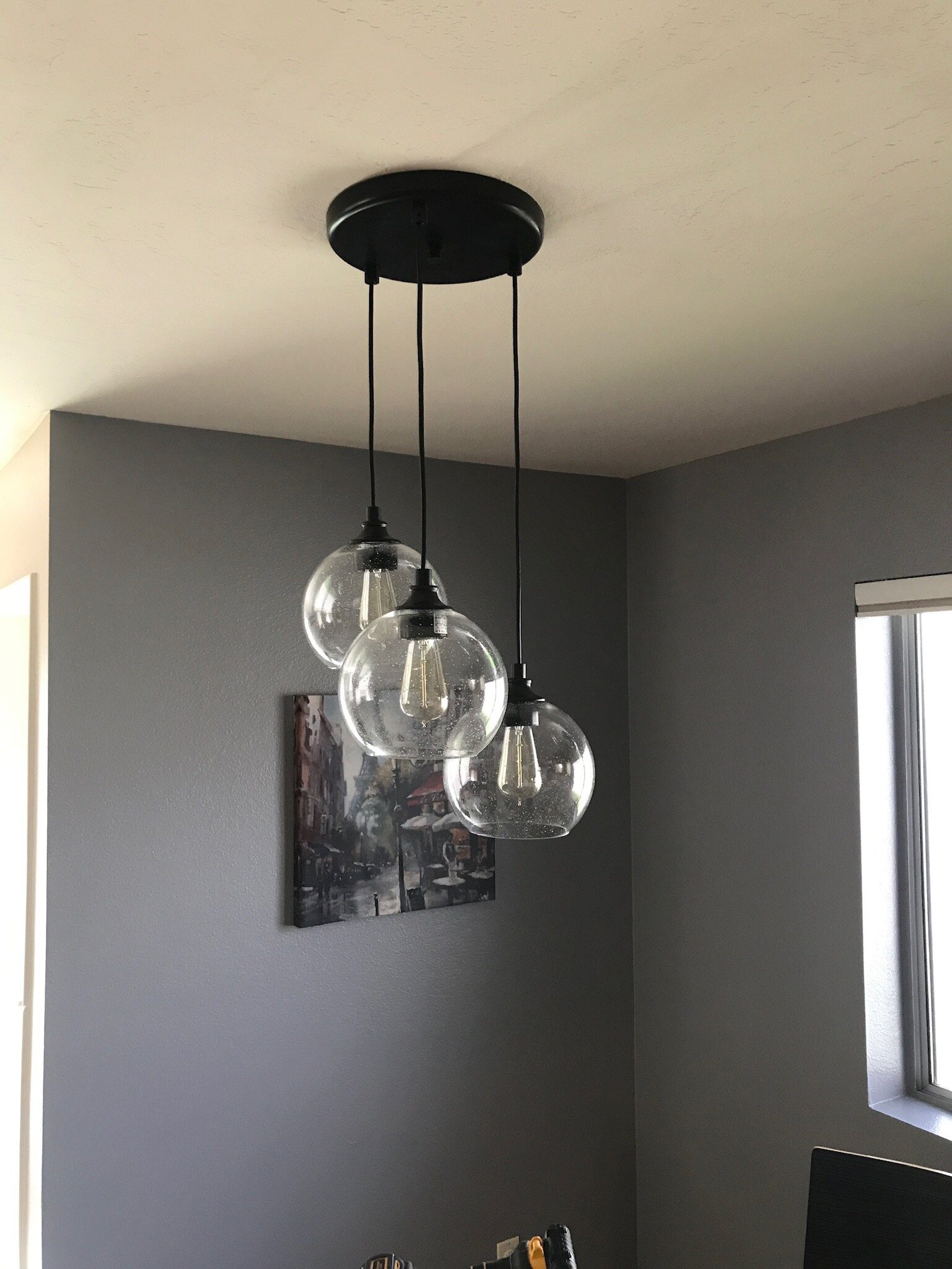 Three clear glass globe pendants hanging from a round black canopy in a gray room