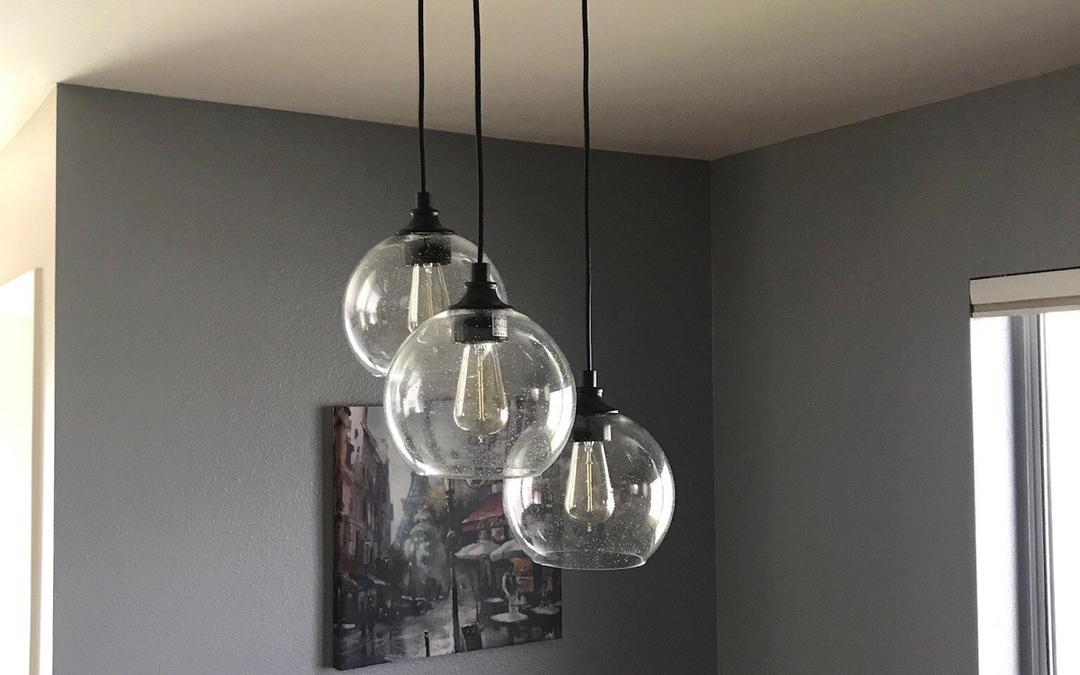 Three clear glass globe pendants hanging from a round black canopy in a gray room