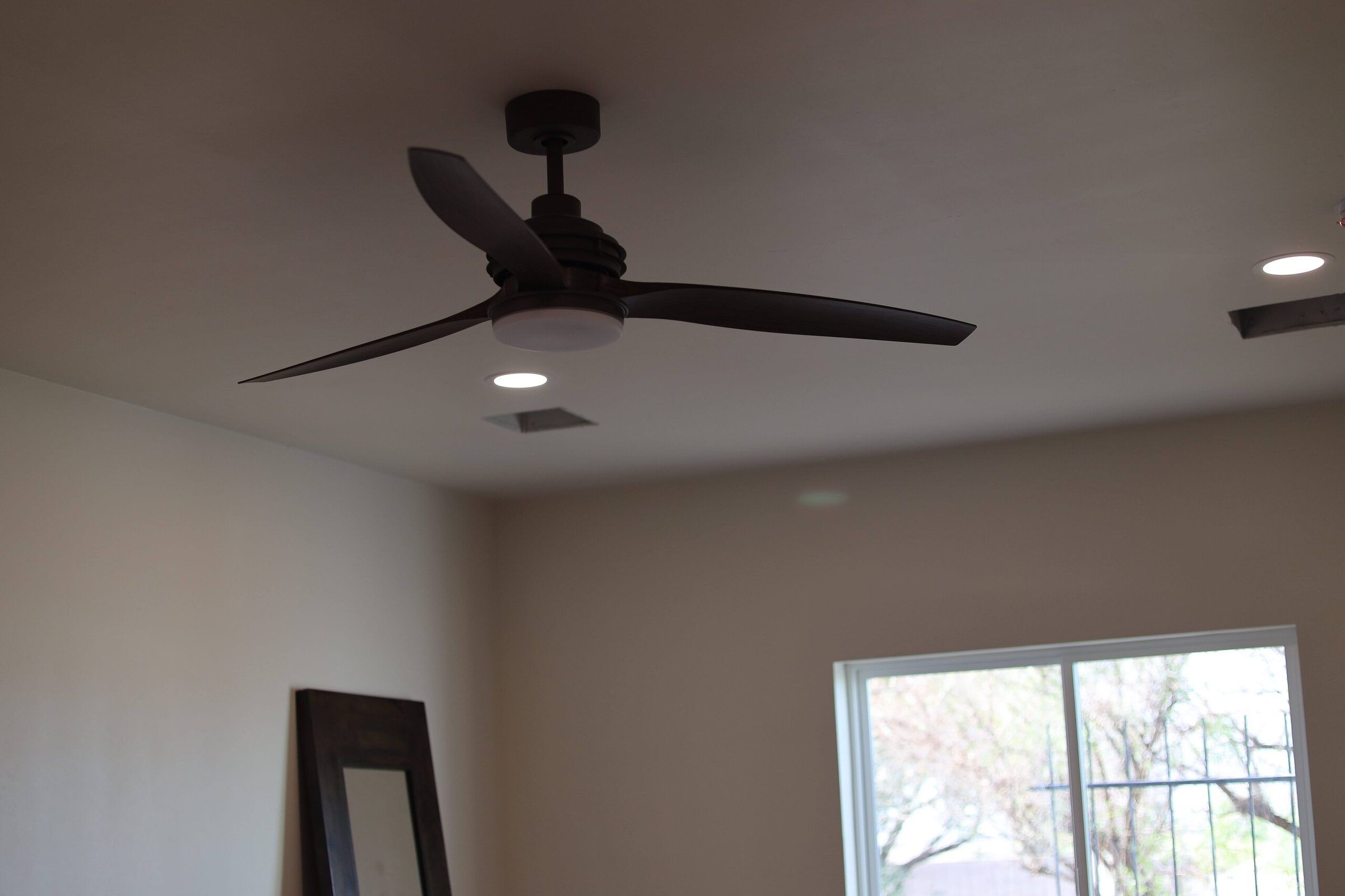 Dark three-blade ceiling fan with light kit and recessed lights in a room with a sliding door