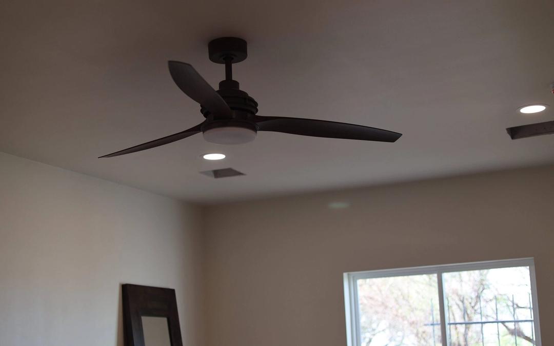 Dark three-blade ceiling fan with light kit and recessed lights in a room with a sliding door