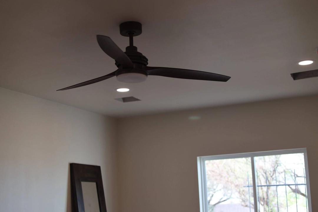 Dark three-blade ceiling fan with light kit and recessed lights in a room with a sliding door