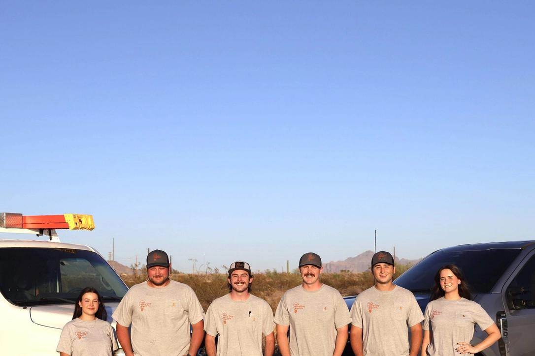 Six Wire Guy Electric team members in company shirts beside vans under a clear evening sky