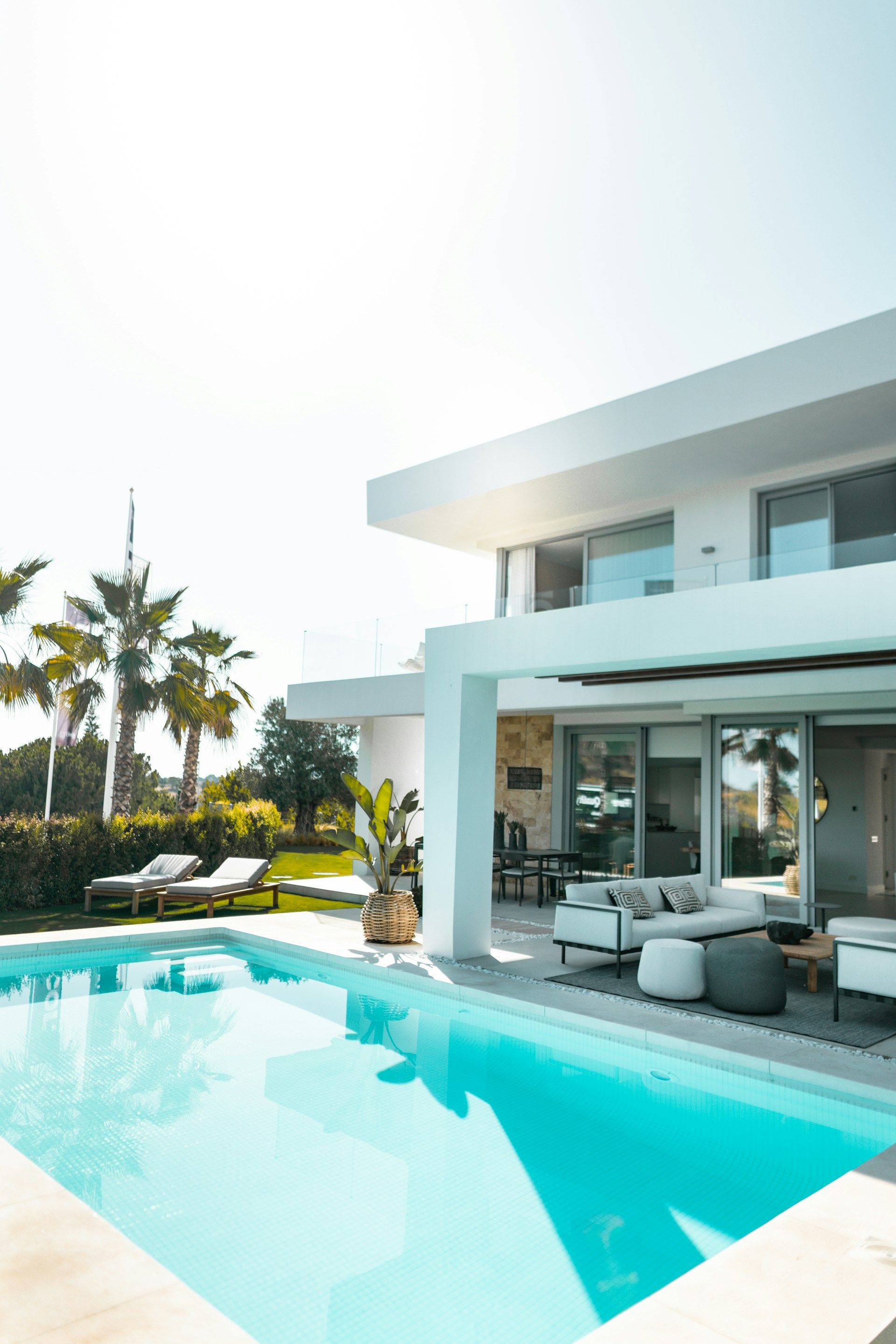 A modern white house with a swimming pool, patio furniture and palm trees