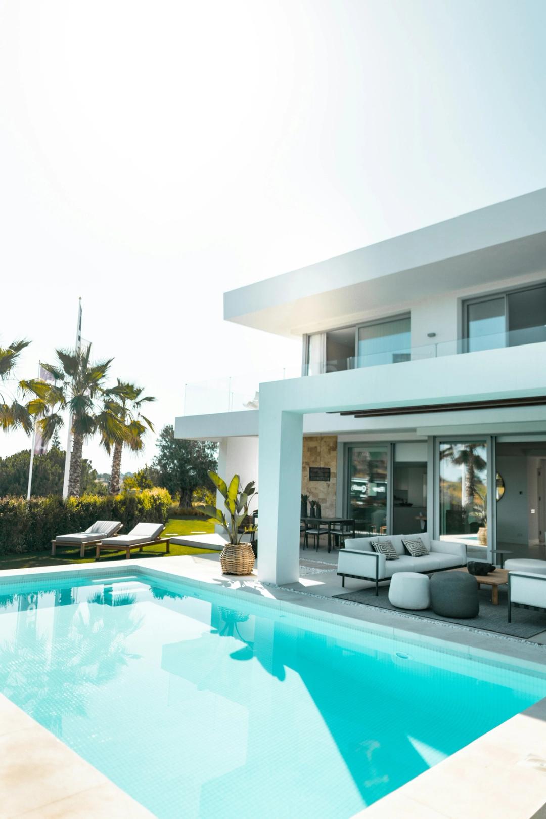 A modern white house with a swimming pool, patio furniture and palm trees