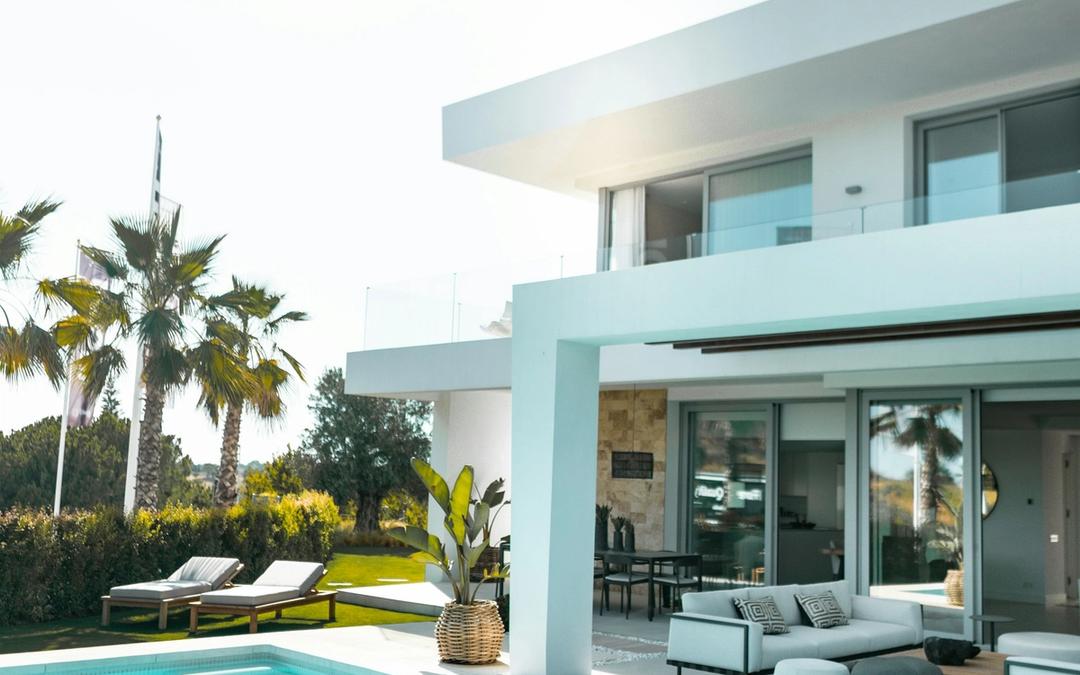 A modern white house with a swimming pool, patio furniture and palm trees