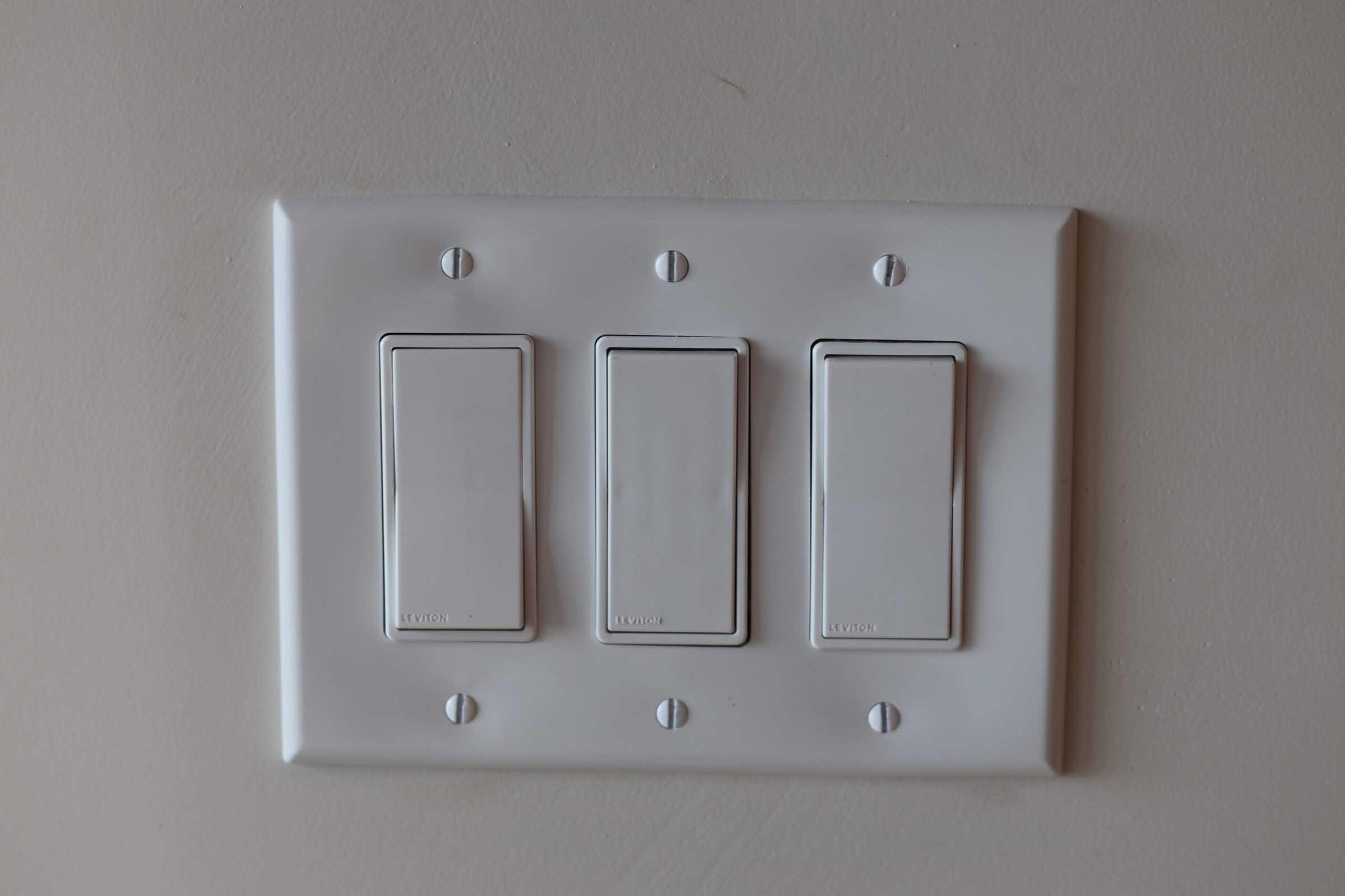 Close-up of a three-gang white rocker switch plate on a gray wall