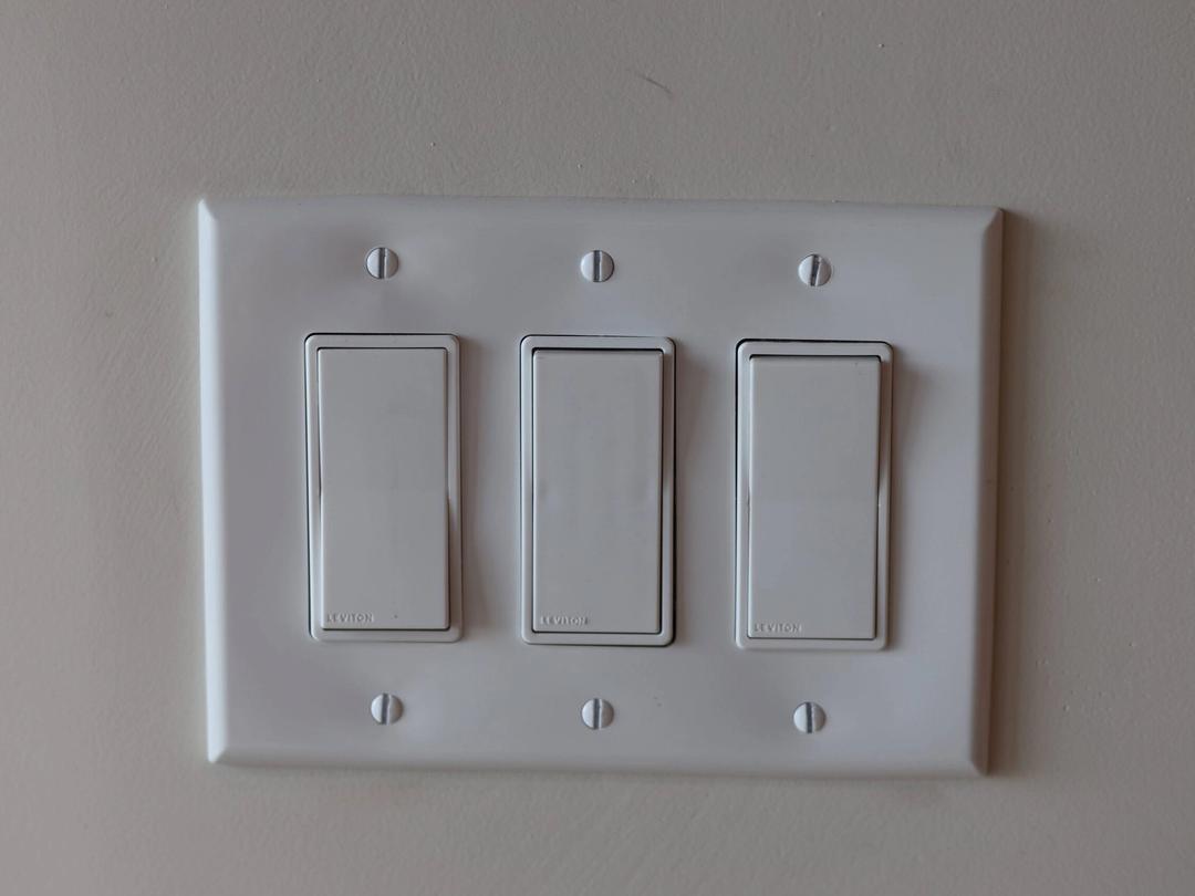 Close-up of a three-gang white rocker switch plate on a gray wall