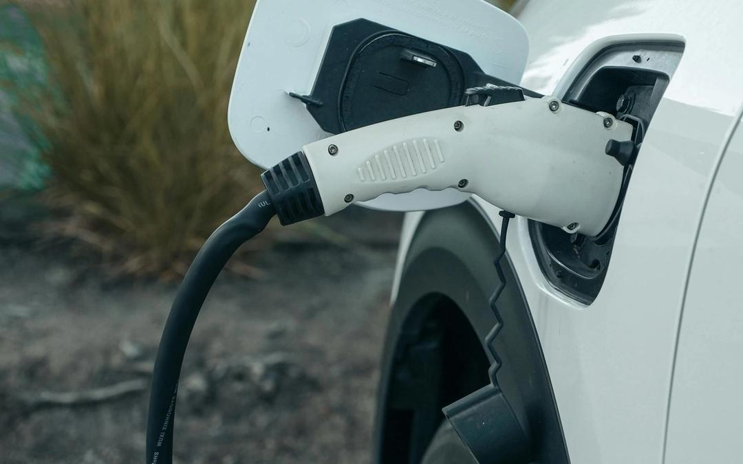 A charging cable plugged into the port of a white electric car parked by desert grasses