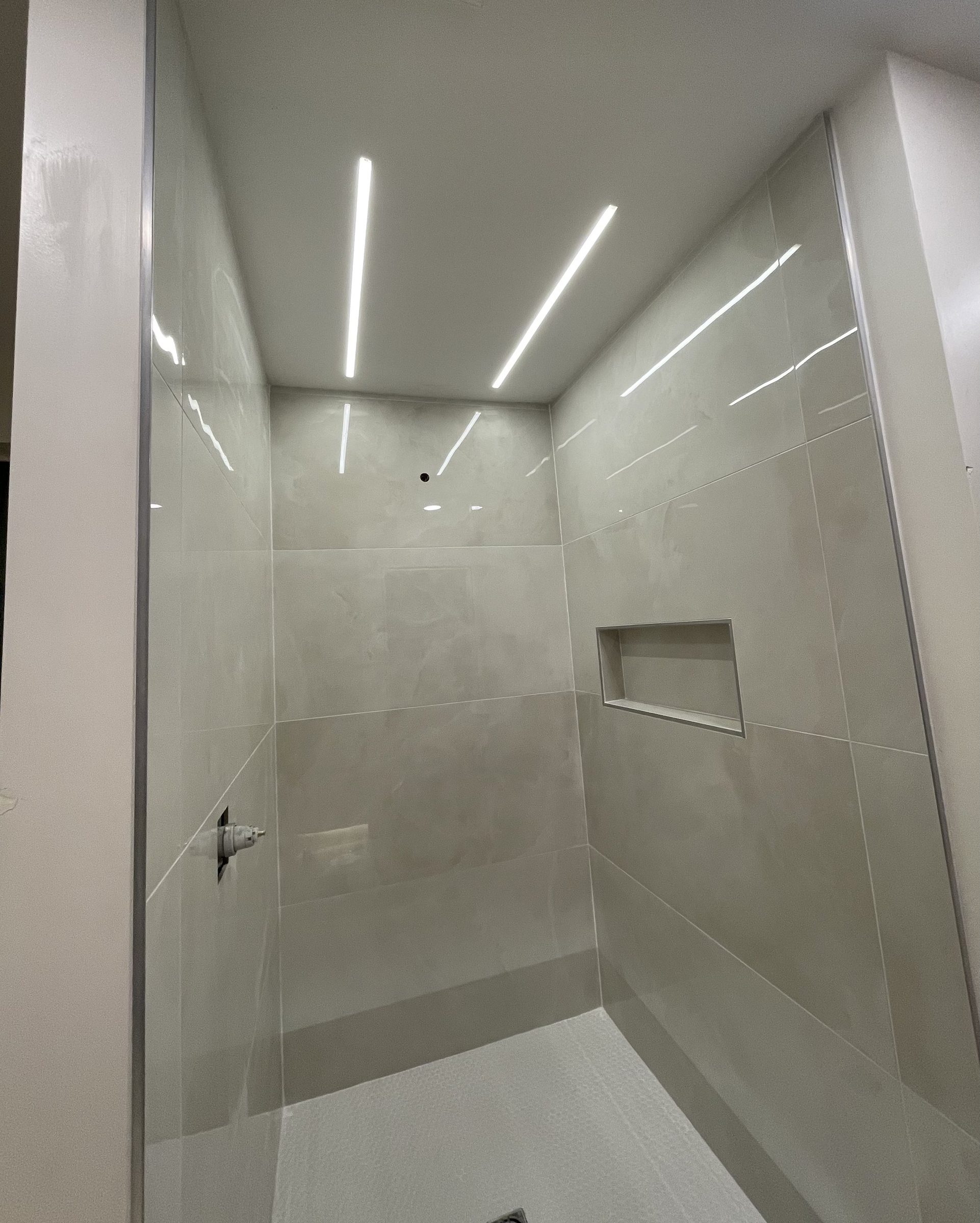 Modern tiled shower with linear LED lights recessed in the ceiling