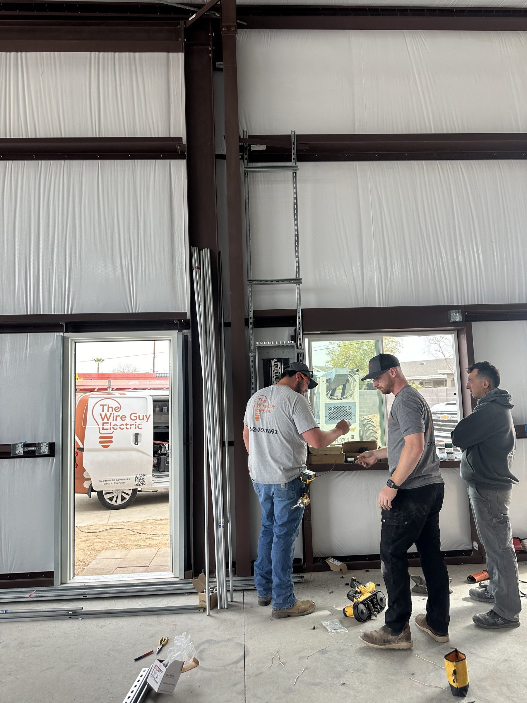 Three electricians planning work inside a metal building with a Wire Guy Electric van outside