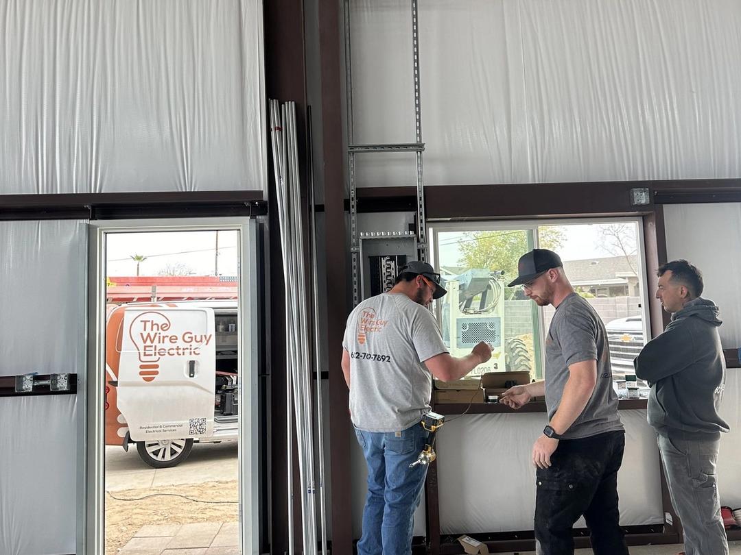Three electricians planning work inside a metal building with a Wire Guy Electric van outside