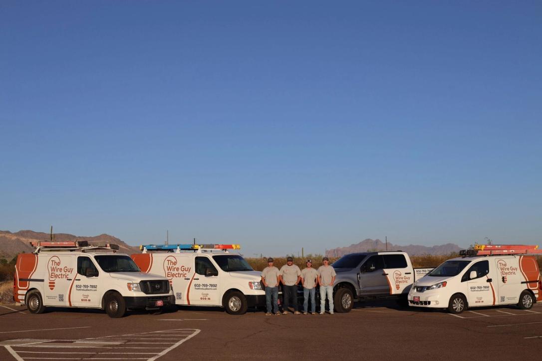 Four Wire Guy Electric technicians standing among the company vans and pickup in the desert