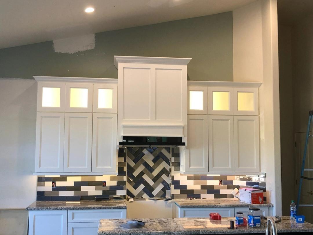 White kitchen with lit glass-front cabinets and a herringbone tile backsplash