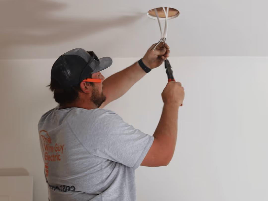 A Wire Guy Electric electrician in safety glasses working wires out of a ceiling opening