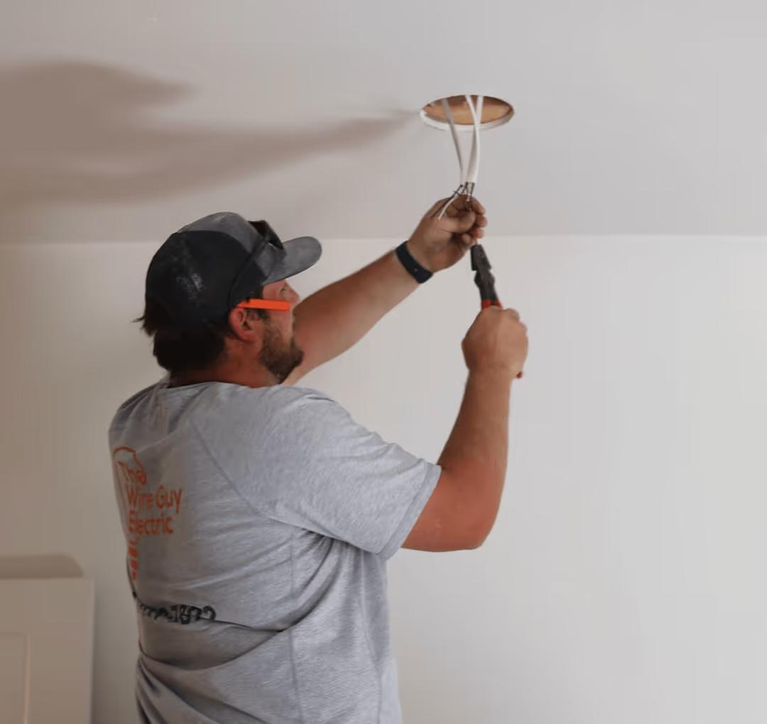 Wire Guy Electric electrician in safety glasses working on wires at a light opening in a ceiling