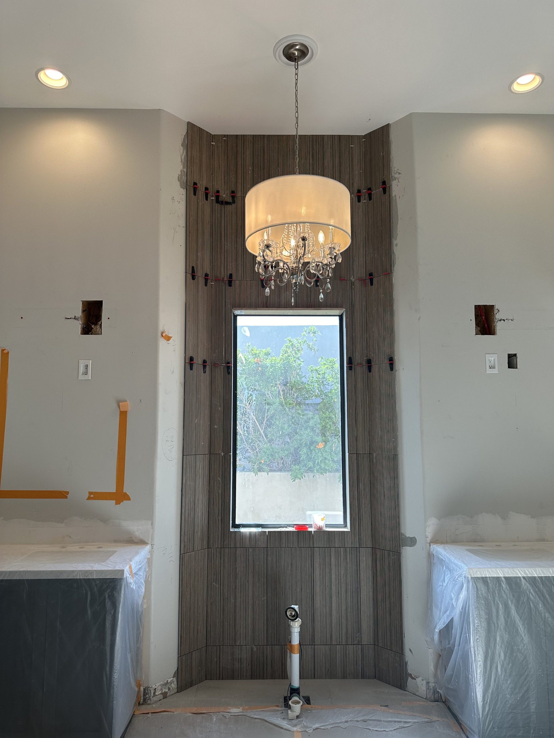 Drum crystal chandelier above a tiled window wall between unfinished bathroom vanities