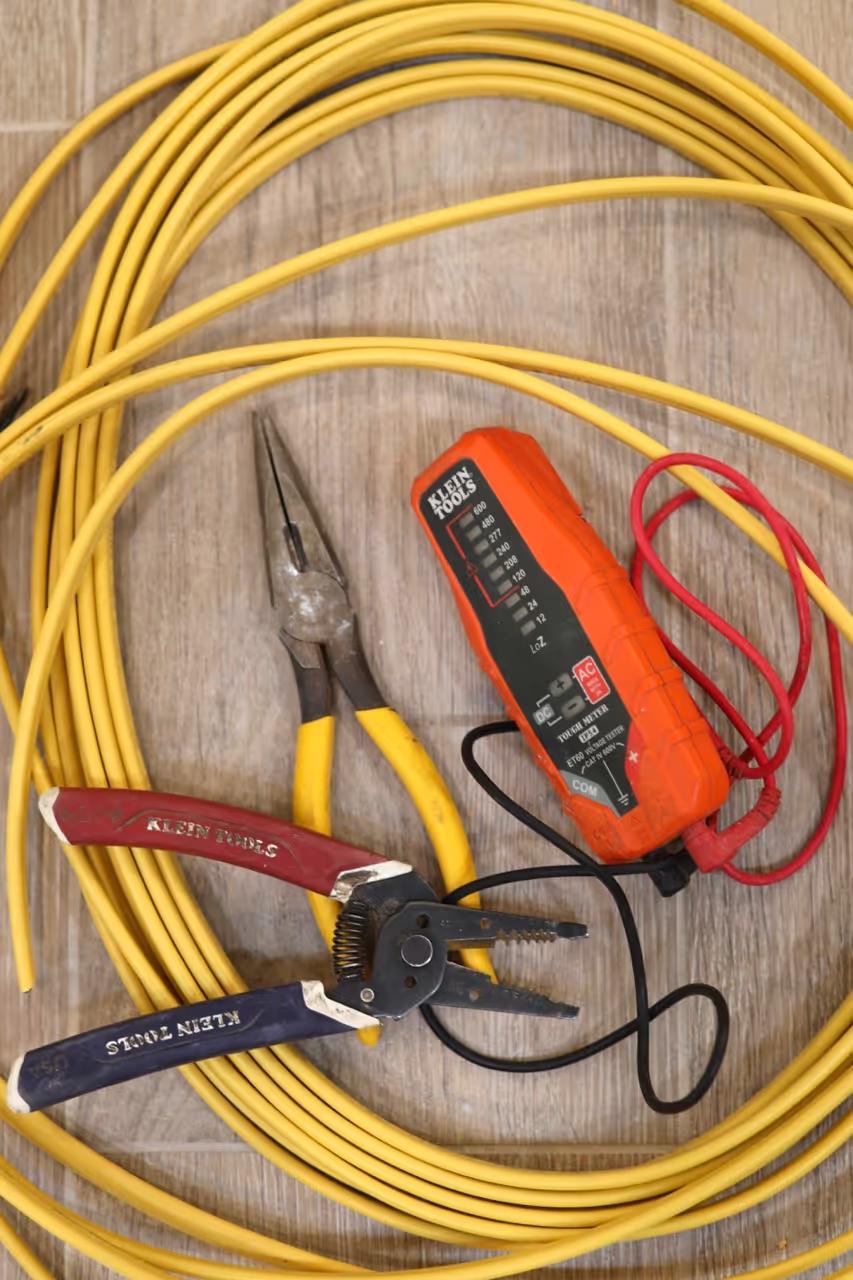 Klein wire strippers, linesman pliers and a voltage tester on a coil of yellow Romex cable