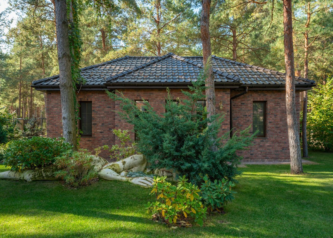 A small brick guest house with a tiled roof among pine trees and a green lawn
