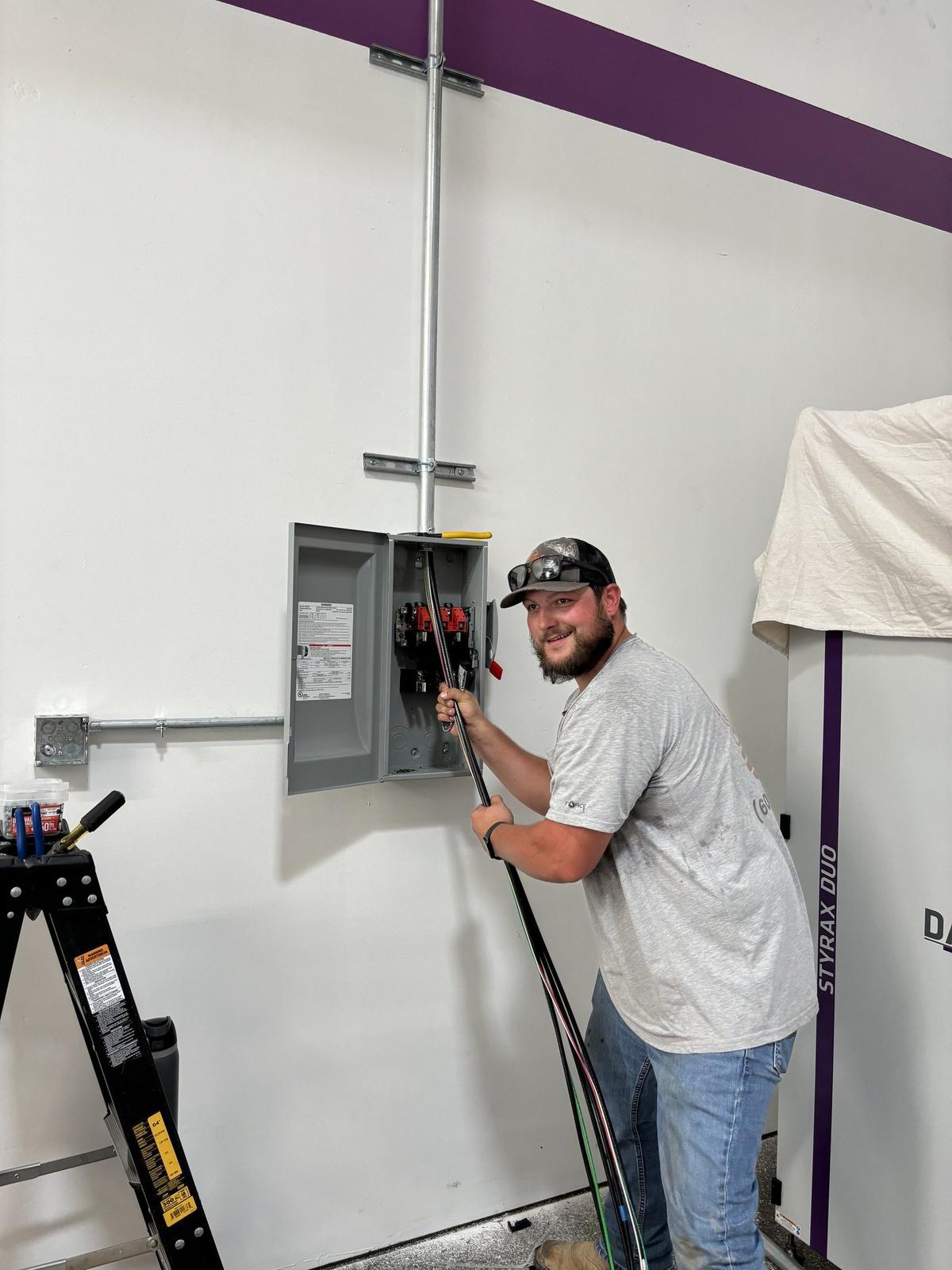 Smiling electrician pulling wire into a disconnect switch on a commercial wall