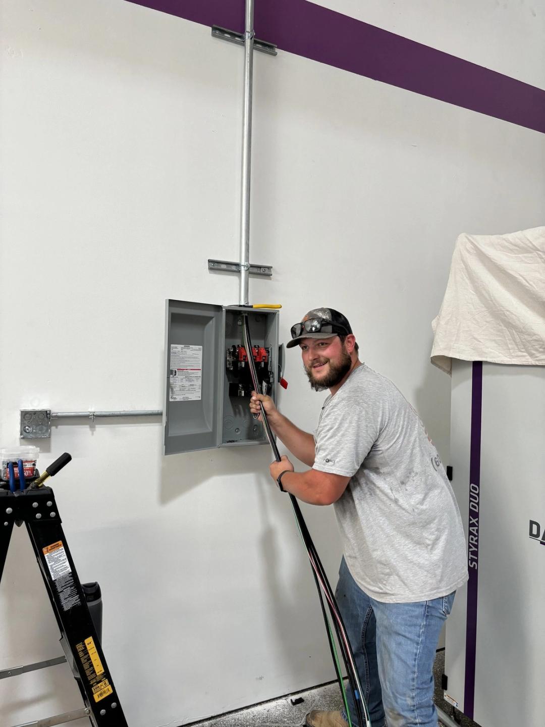 Smiling electrician pulling wire into a disconnect switch on a commercial wall