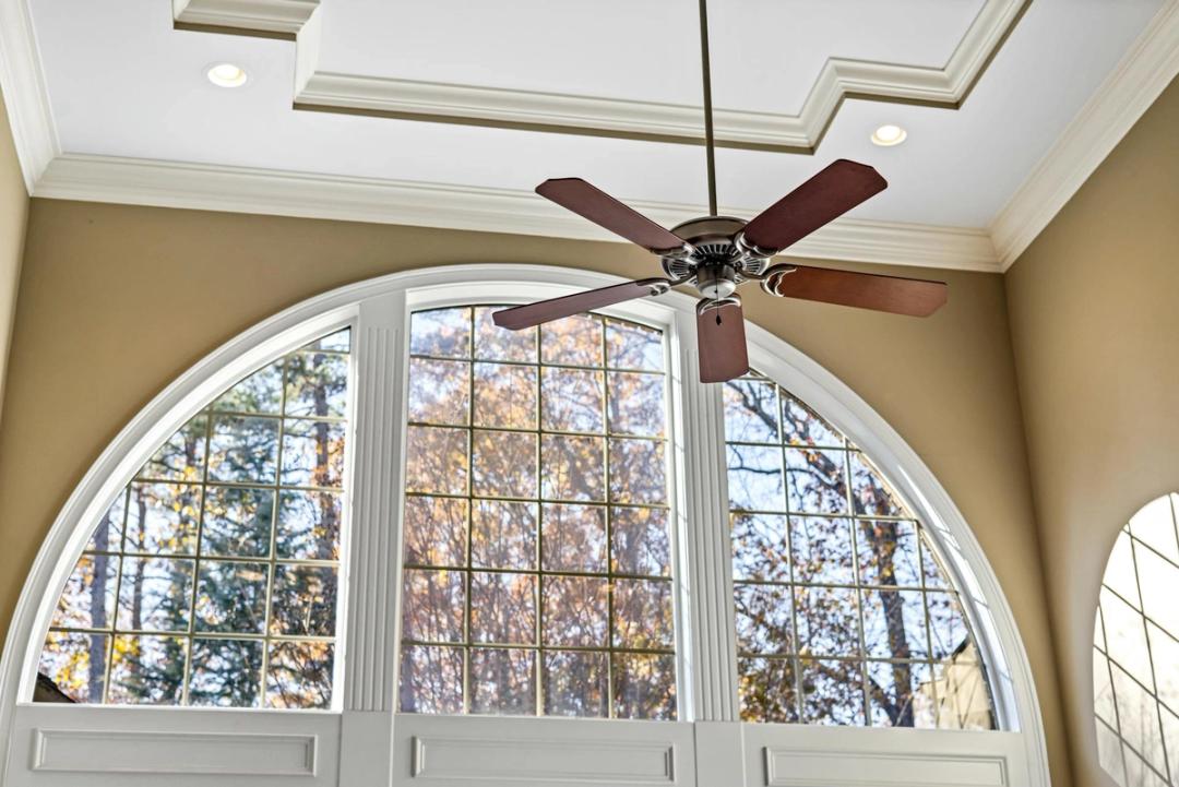 A five-blade ceiling fan under a coffered ceiling, above a tall arched window