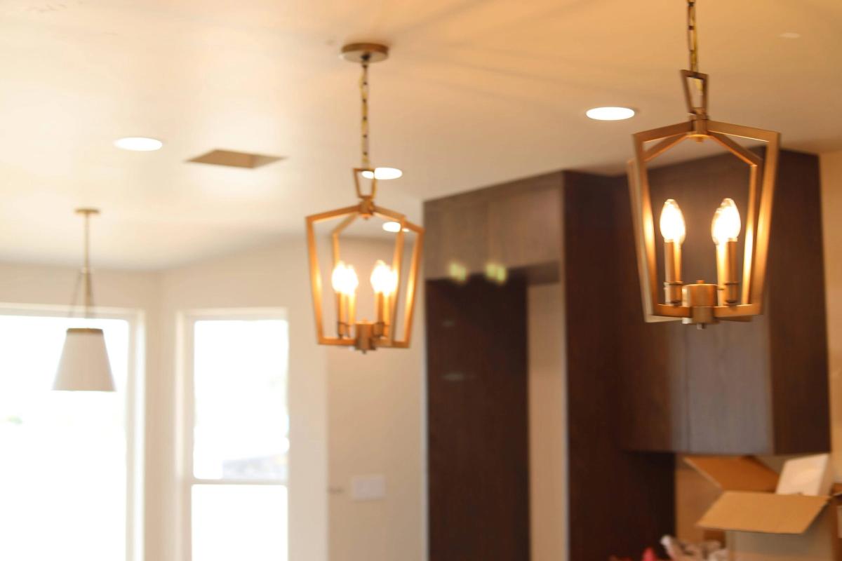 Warm close view of lit brass lantern pendants with candle bulbs, kitchen softly blurred behind