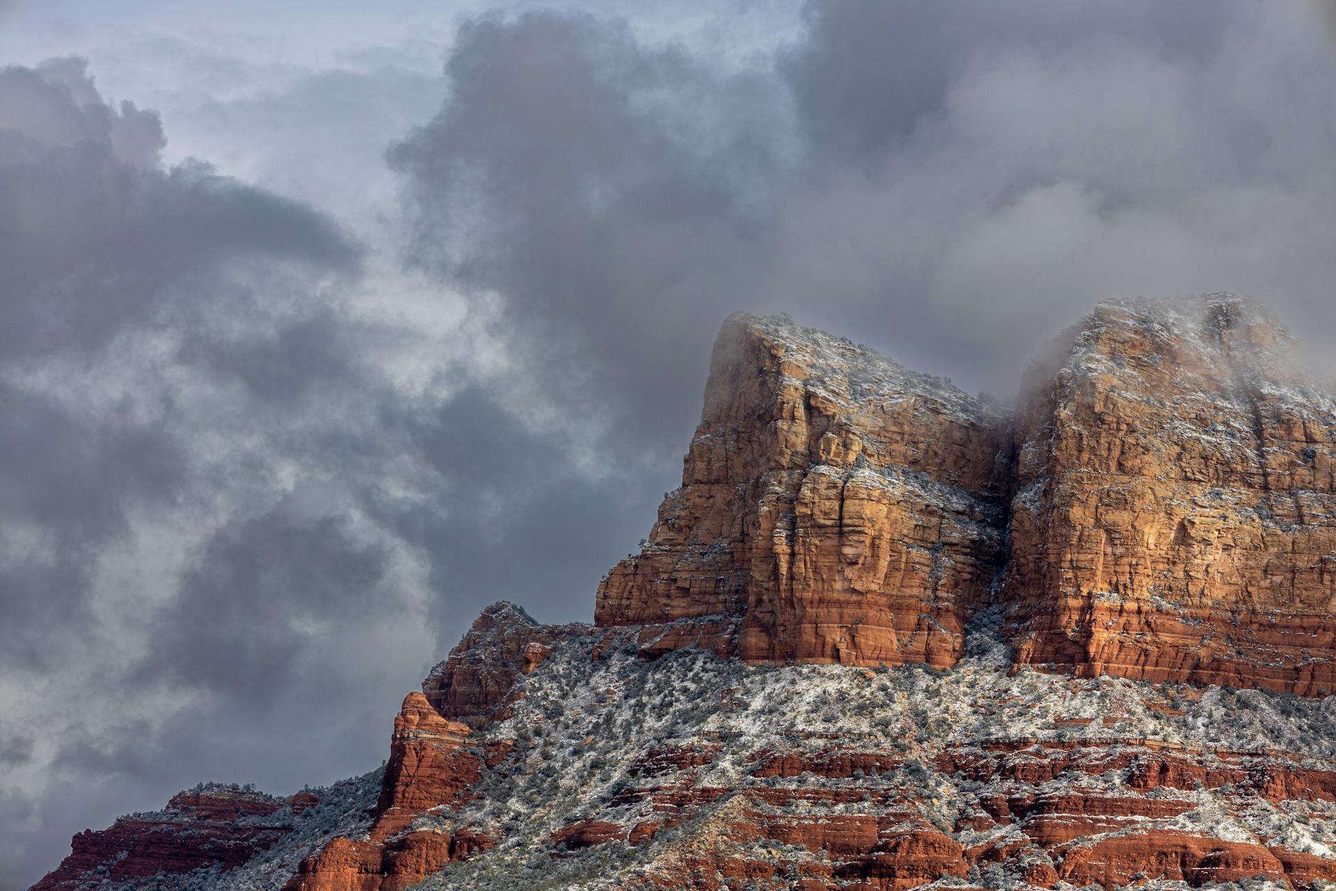 Red rock buttes dusted with snow under heavy gray clouds