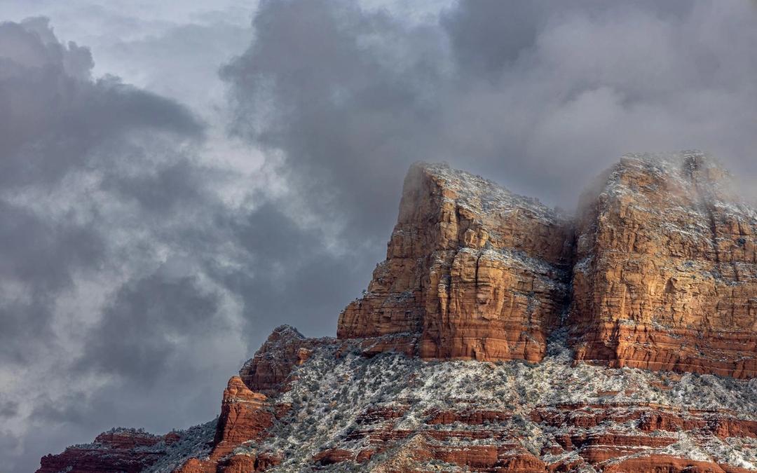 Red rock buttes dusted with snow under heavy gray clouds