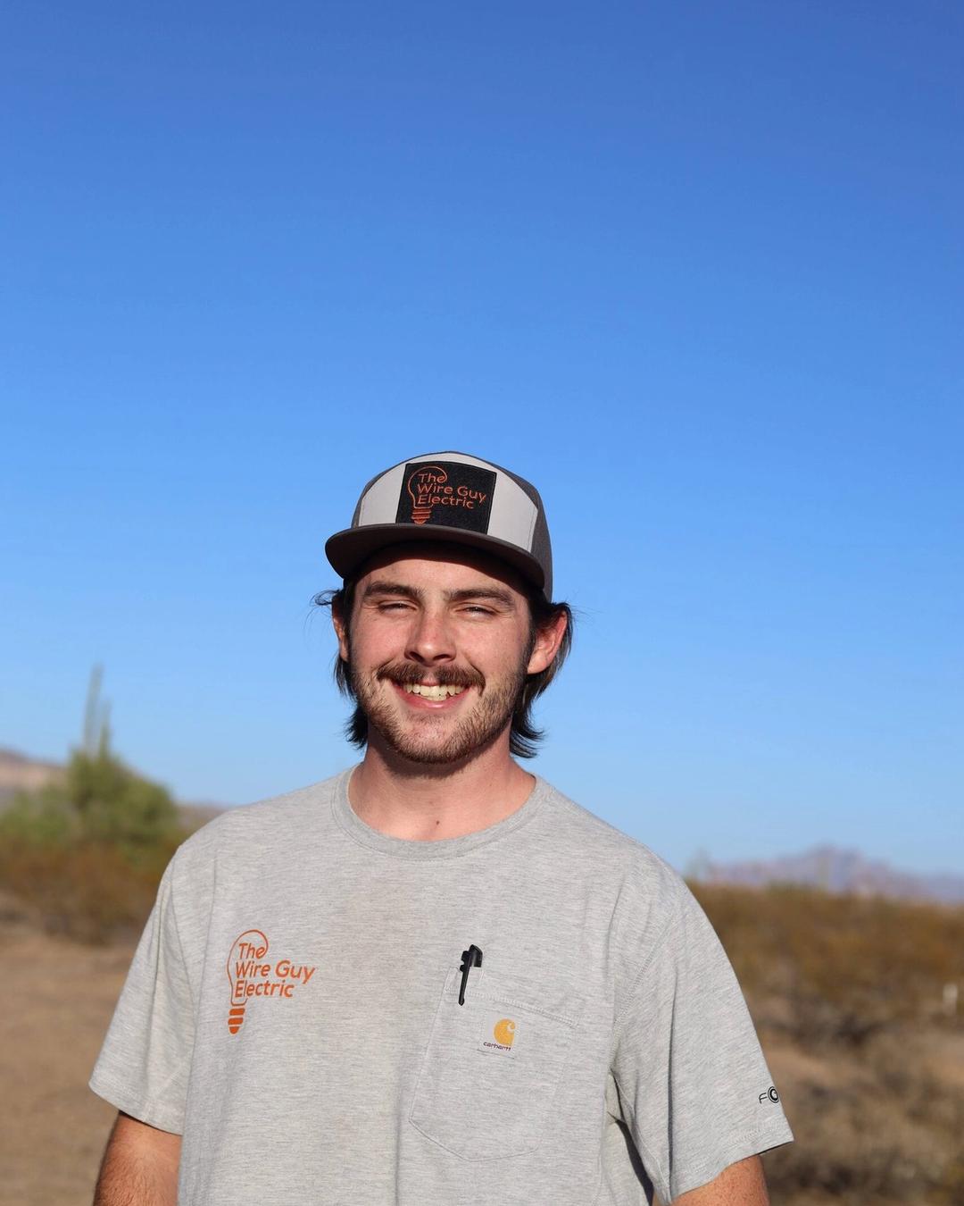 Grinning technician in a Wire Guy Electric cap and shirt against a blue desert sky