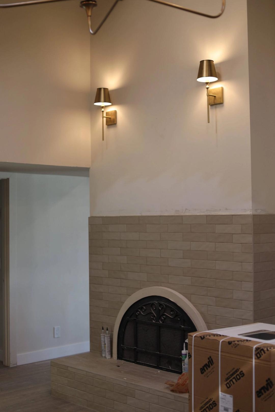 Two brass wall sconces glowing above a tiled fireplace