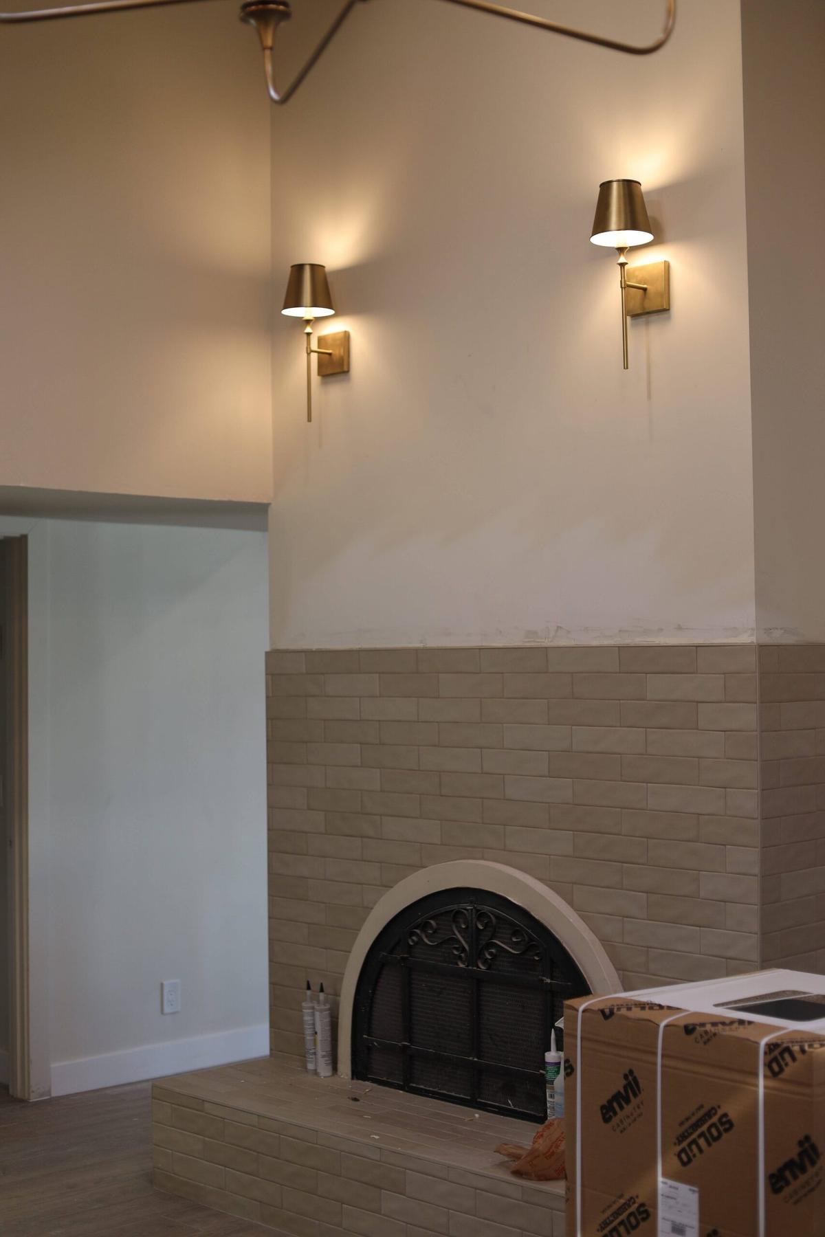 Two brass wall sconces glowing above a tiled fireplace