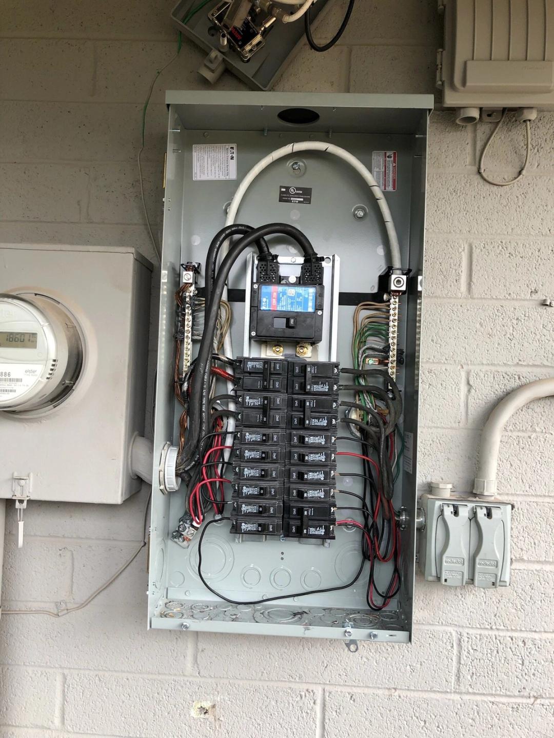 Neatly wired new Eaton breaker panel with the cover off next to a meter