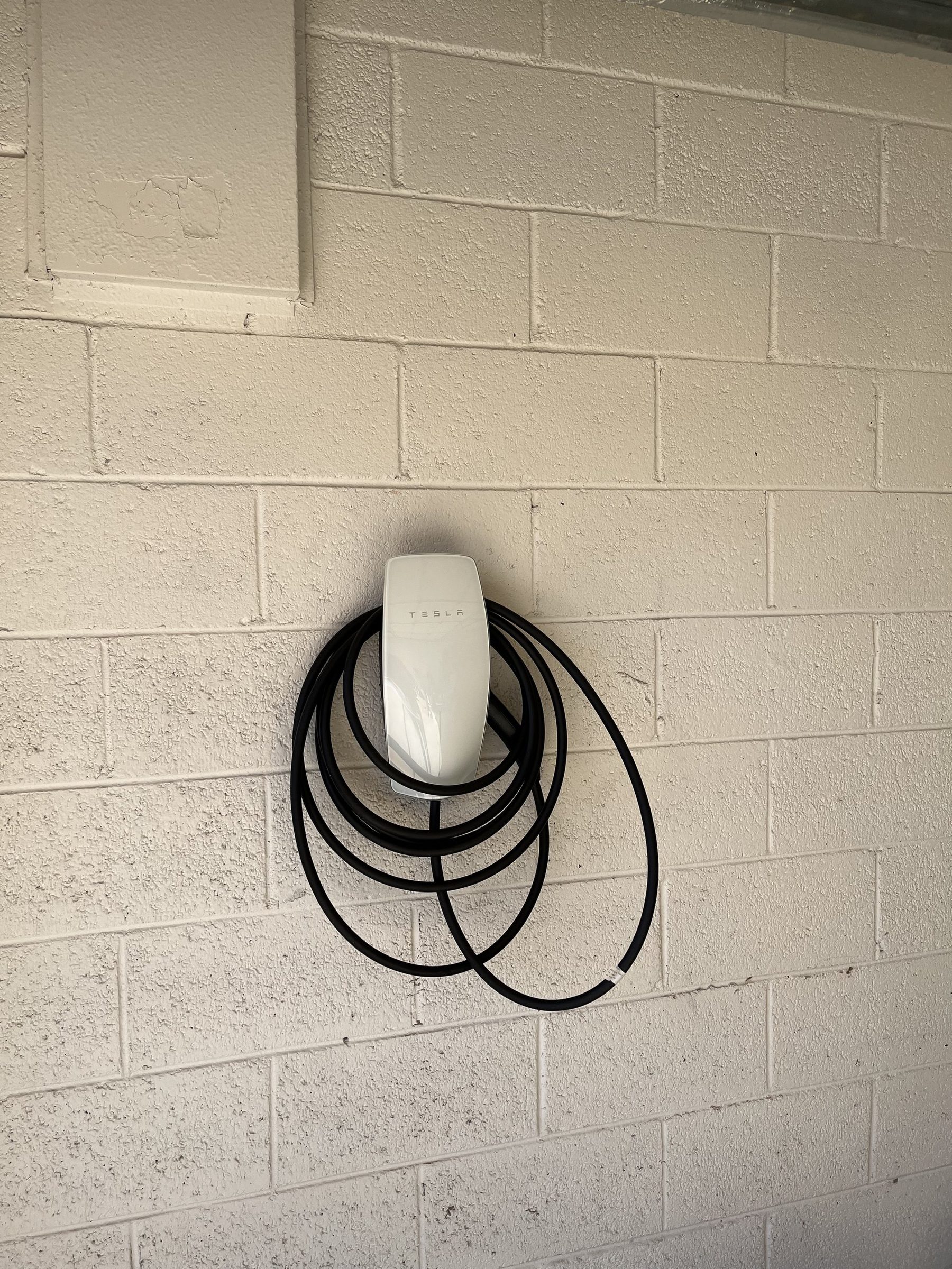 Tesla wall connector with coiled cable mounted on a painted block wall