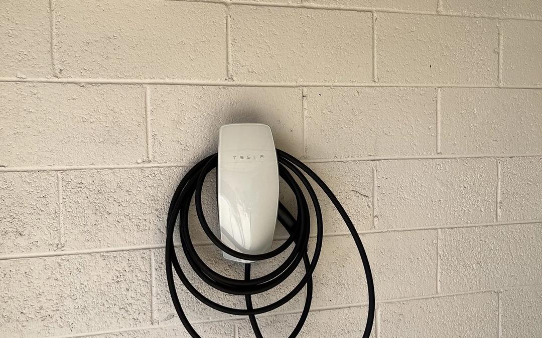 Tesla wall connector with coiled cable mounted on a painted block wall