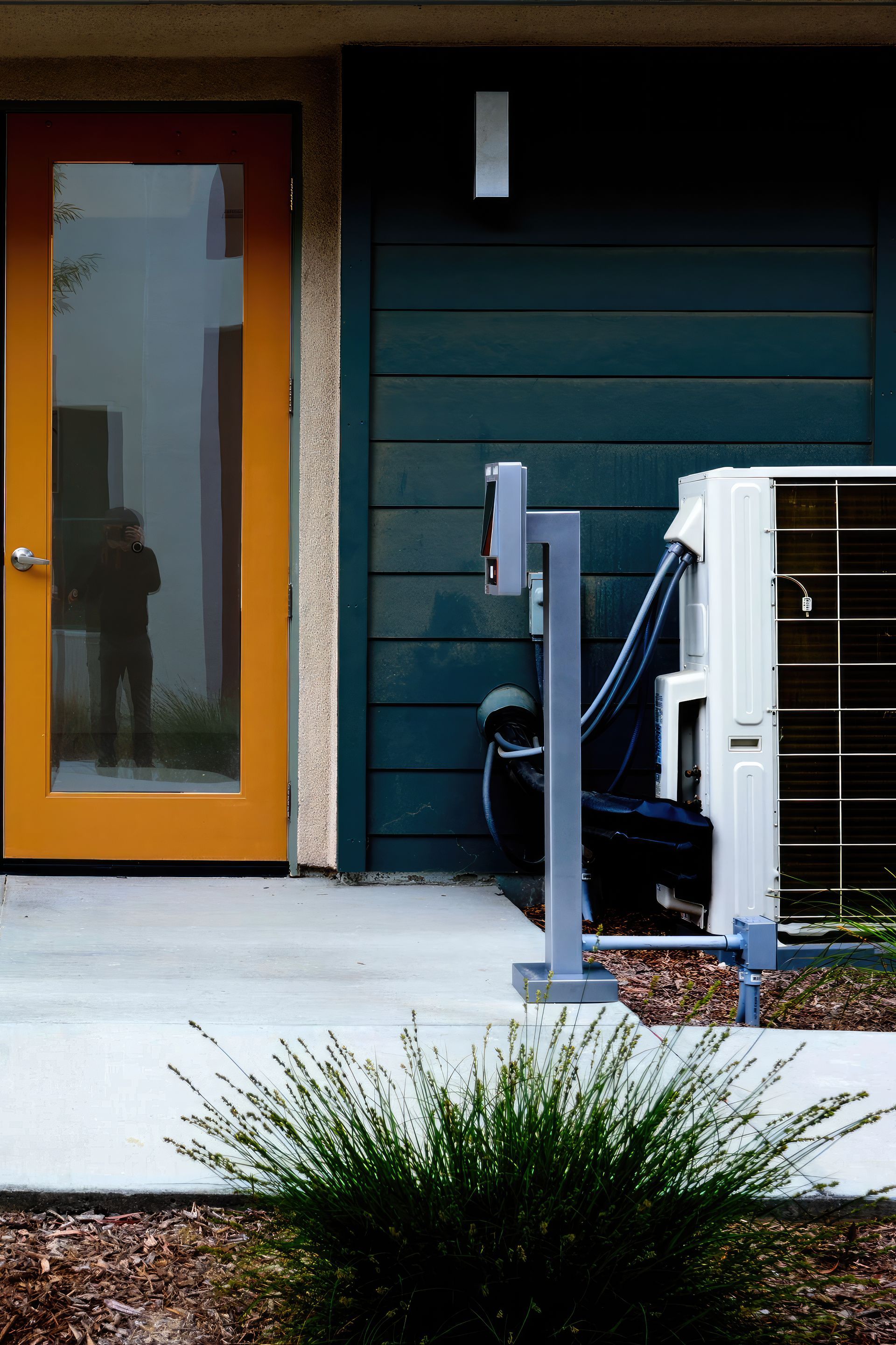 An outdoor air conditioning unit and a charging post beside the front door of a dark-sided home