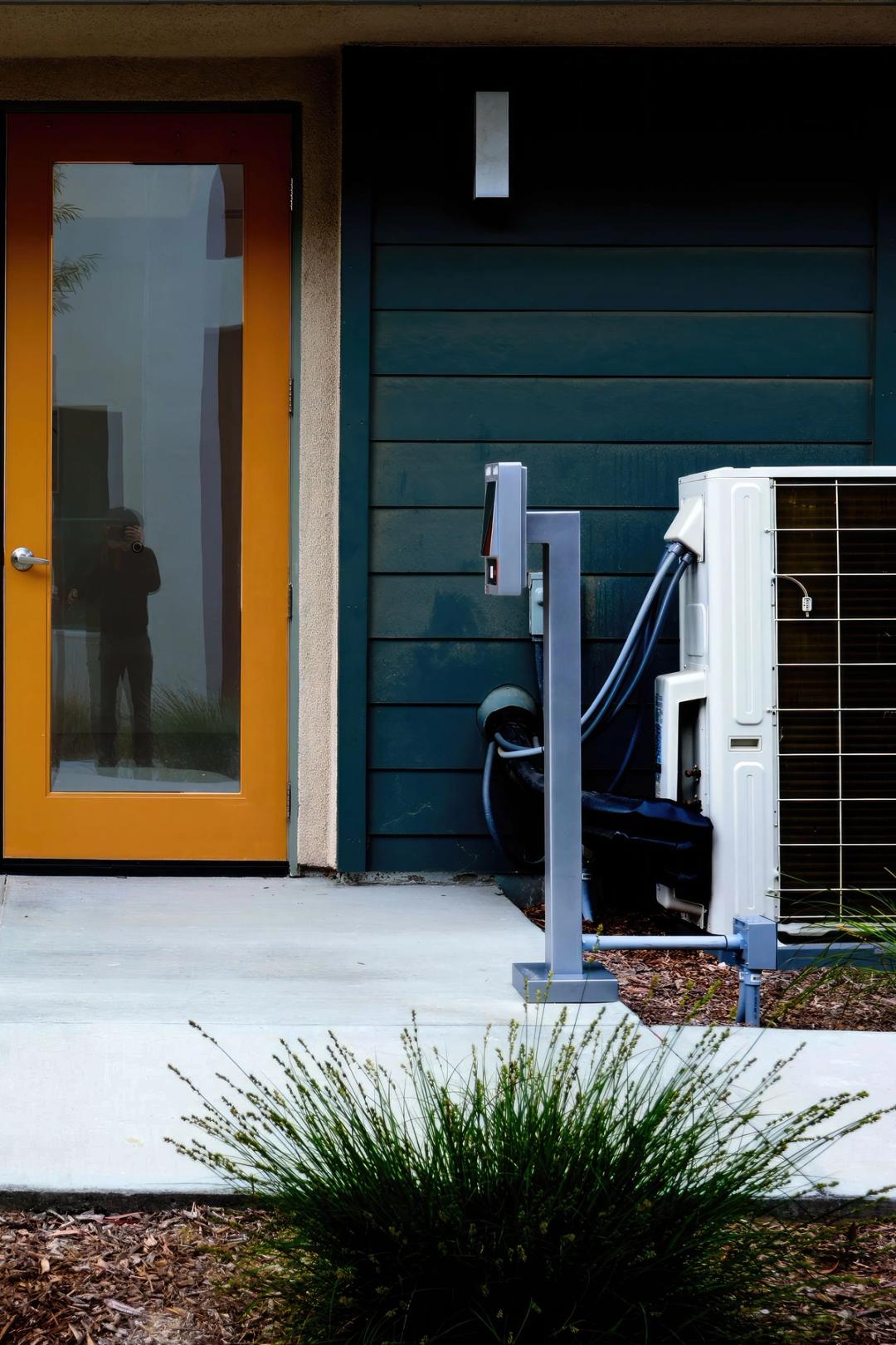 An outdoor air conditioning unit and a charging post beside the front door of a dark-sided home