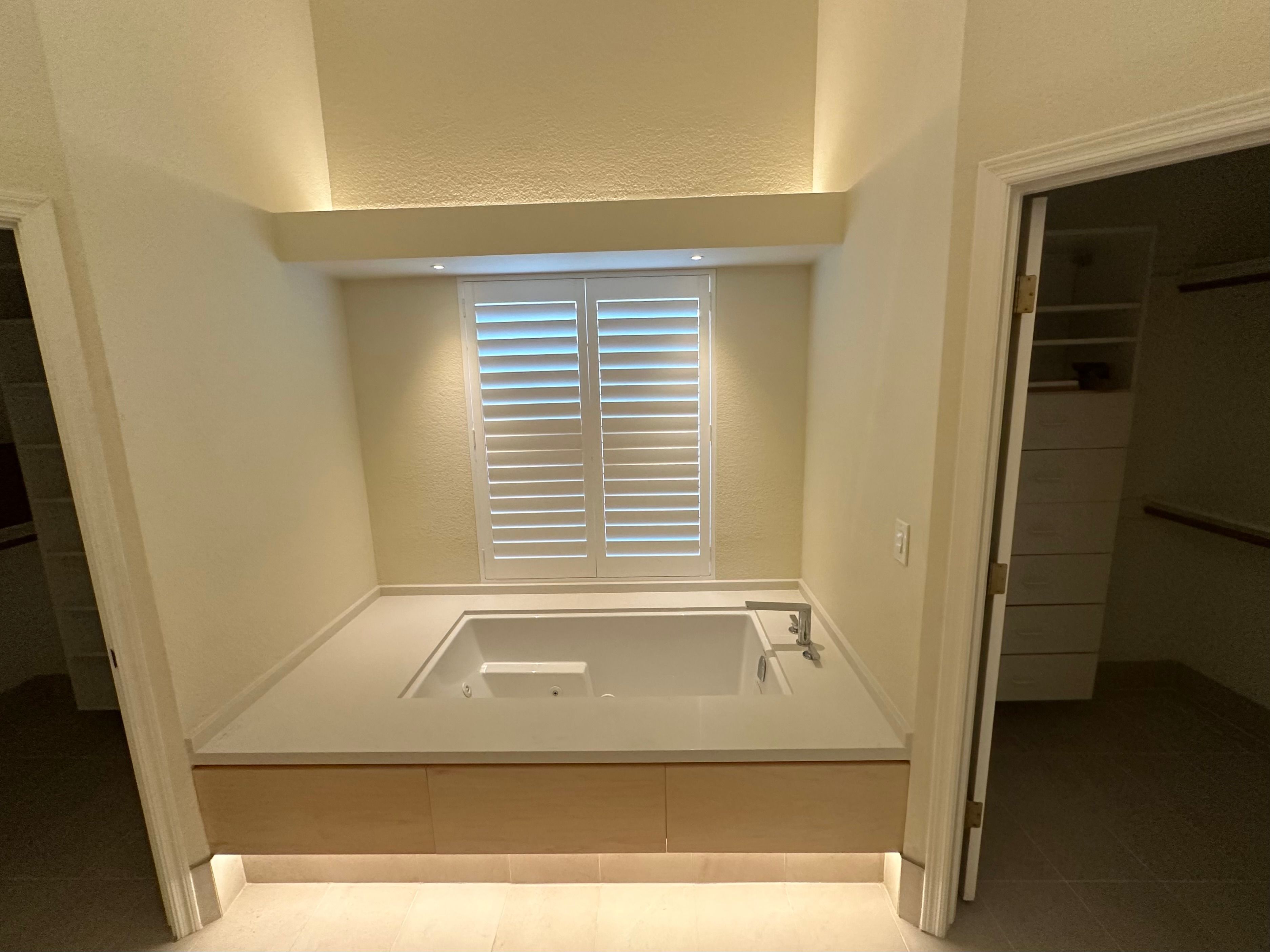 Soaking tub alcove lit by LED cove and toe-kick lighting below plantation shutters