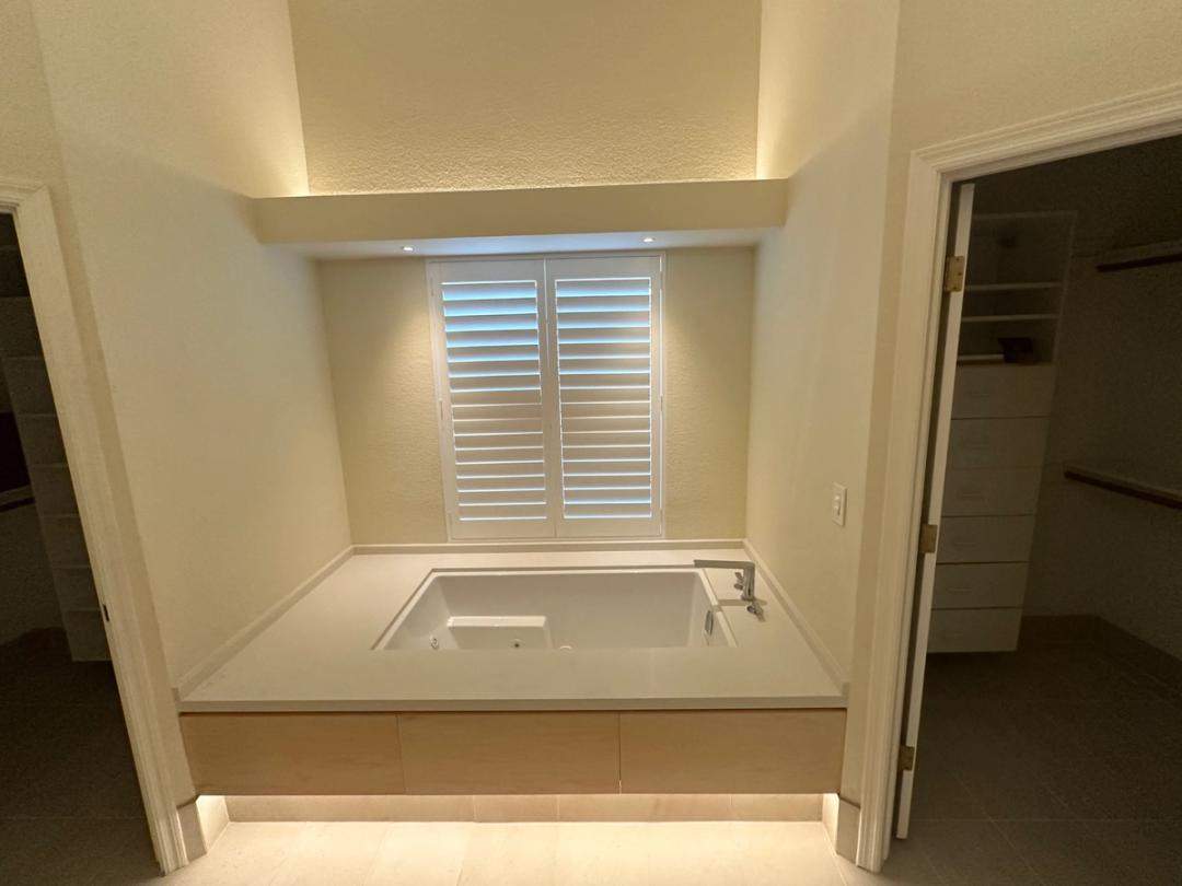 Soaking tub alcove lit by LED cove and toe-kick lighting below plantation shutters