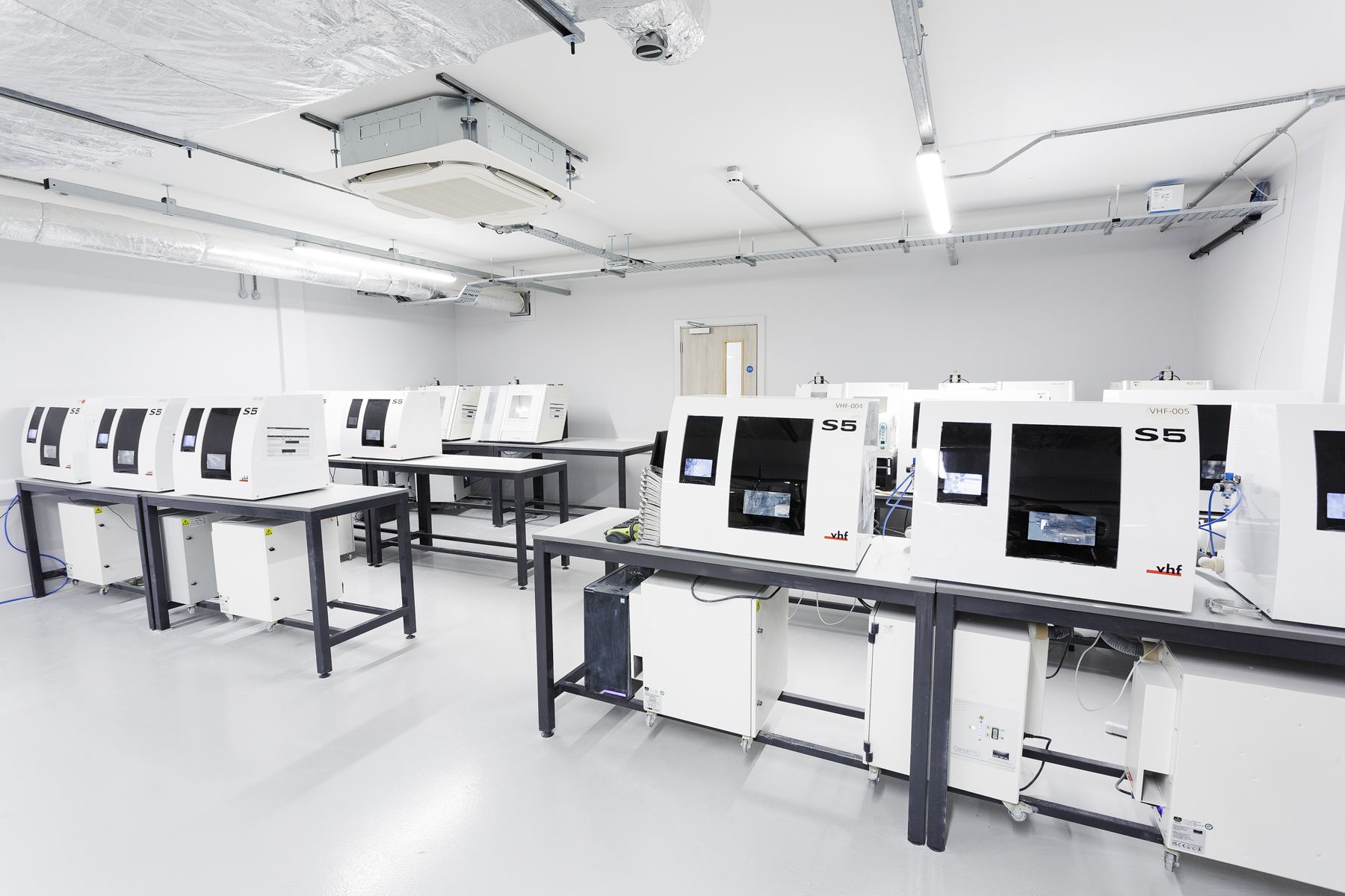 A modern dental laboratory workspace featuring multiple S5 milling units and automated dental equipment arranged on work tables for digital crown and restoration fabrication.
