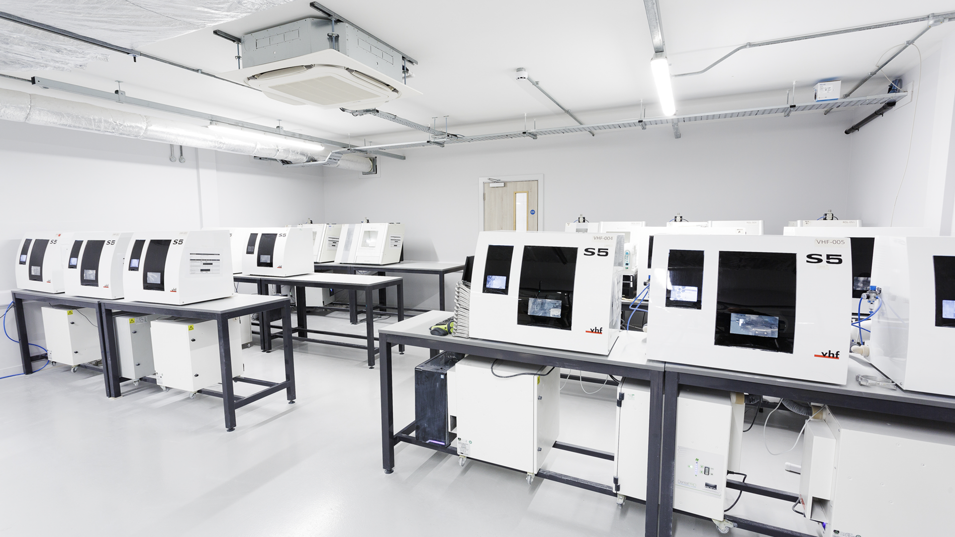 A modern dental laboratory workspace featuring multiple S5 milling units and automated dental equipment arranged on work tables for digital crown and restoration fabrication.