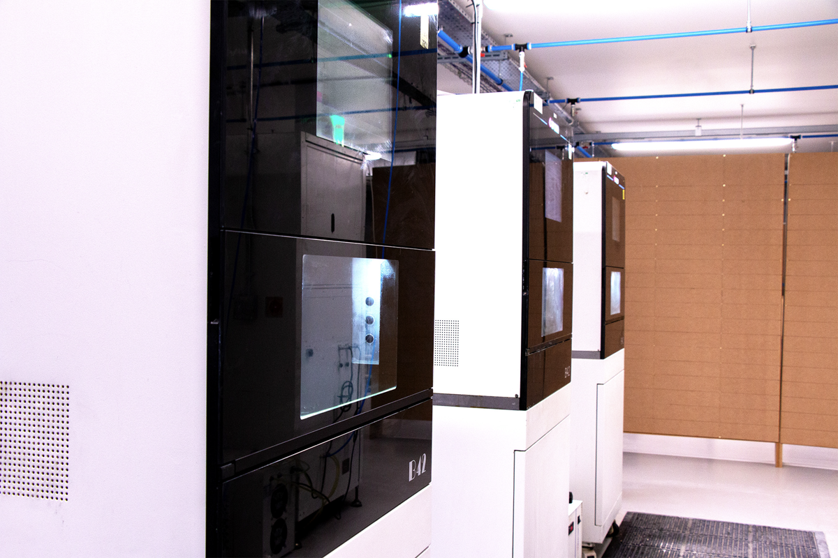 A row of advanced dental milling machines with black and white enclosures and illuminated control panels installed in a modern dental laboratory workspace.