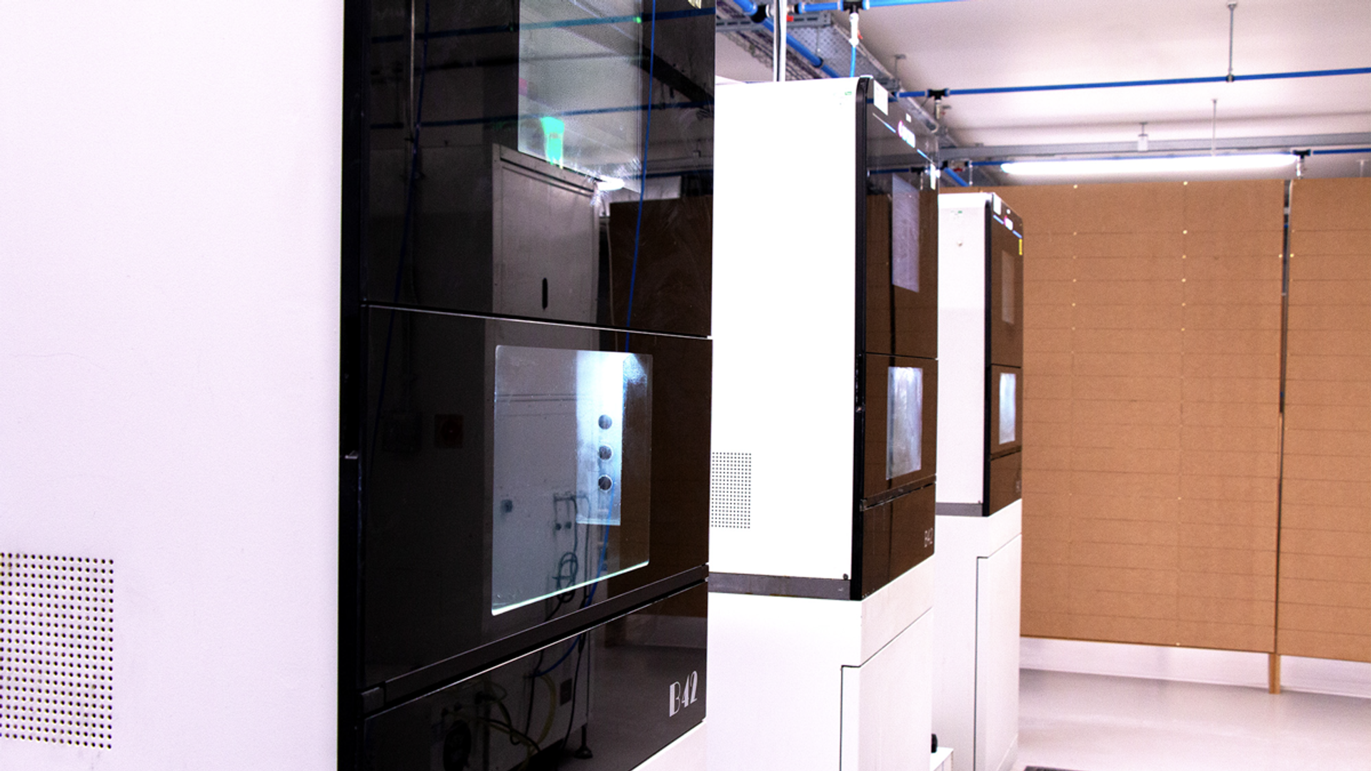 A row of advanced dental milling machines with black and white enclosures and illuminated control panels installed in a modern dental laboratory workspace.