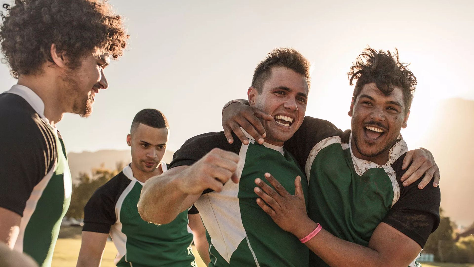 Image of four male rugby players dressed in green, looking jovial