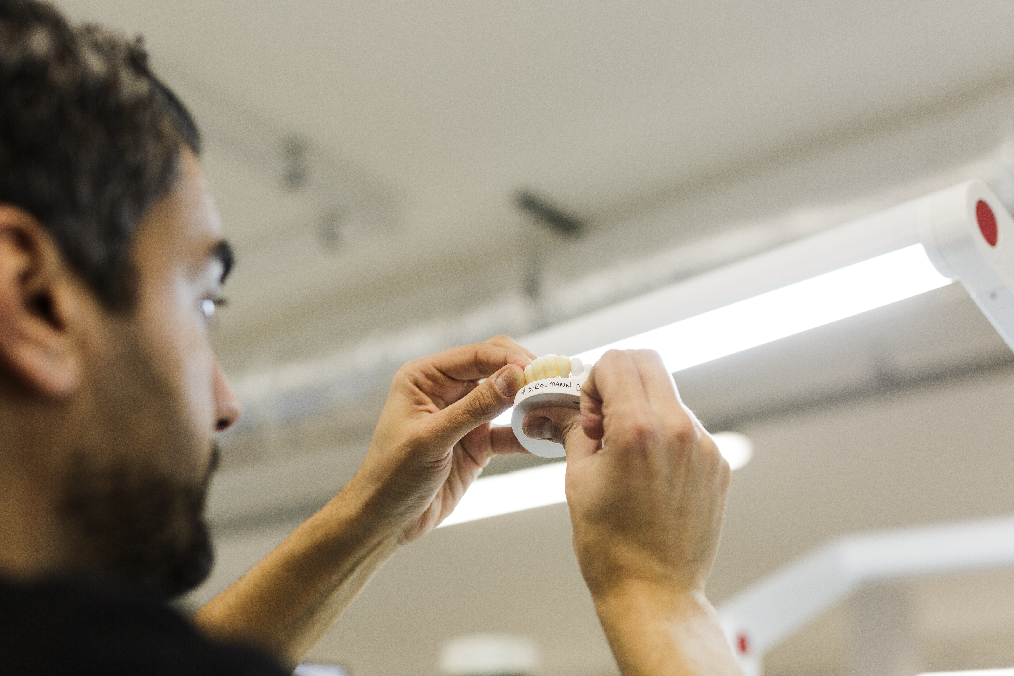 A dental laboratory technician inspects a tooth shade guide under bright lighting to match porcelain crown or veneer color during prosthodontic restoration work.