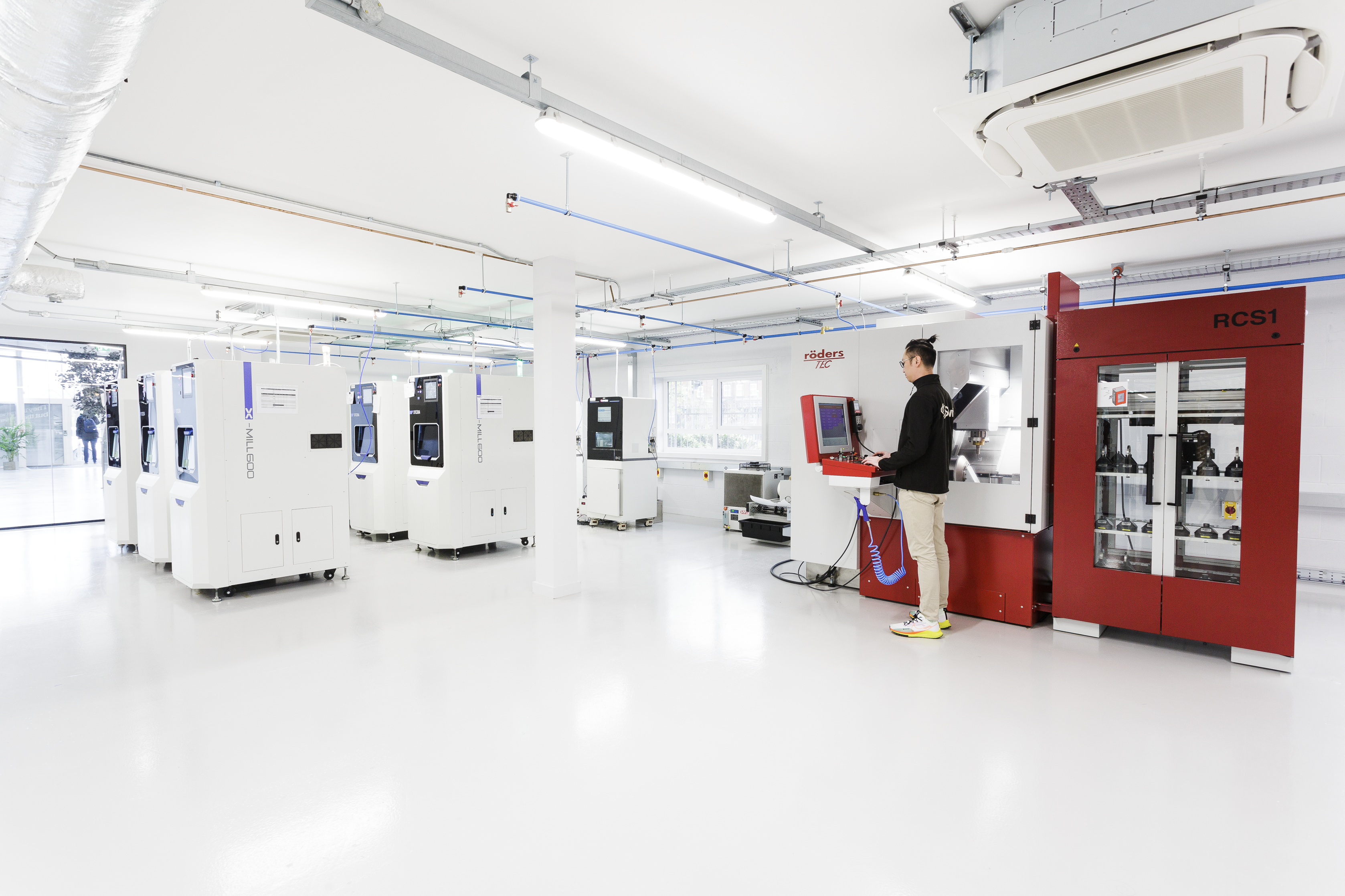 A technician operates an advanced red RCS1 milling machine in a state-of-the-art dental laboratory filled with multiple white CAD/CAM milling units used for fabricating dental restorations.