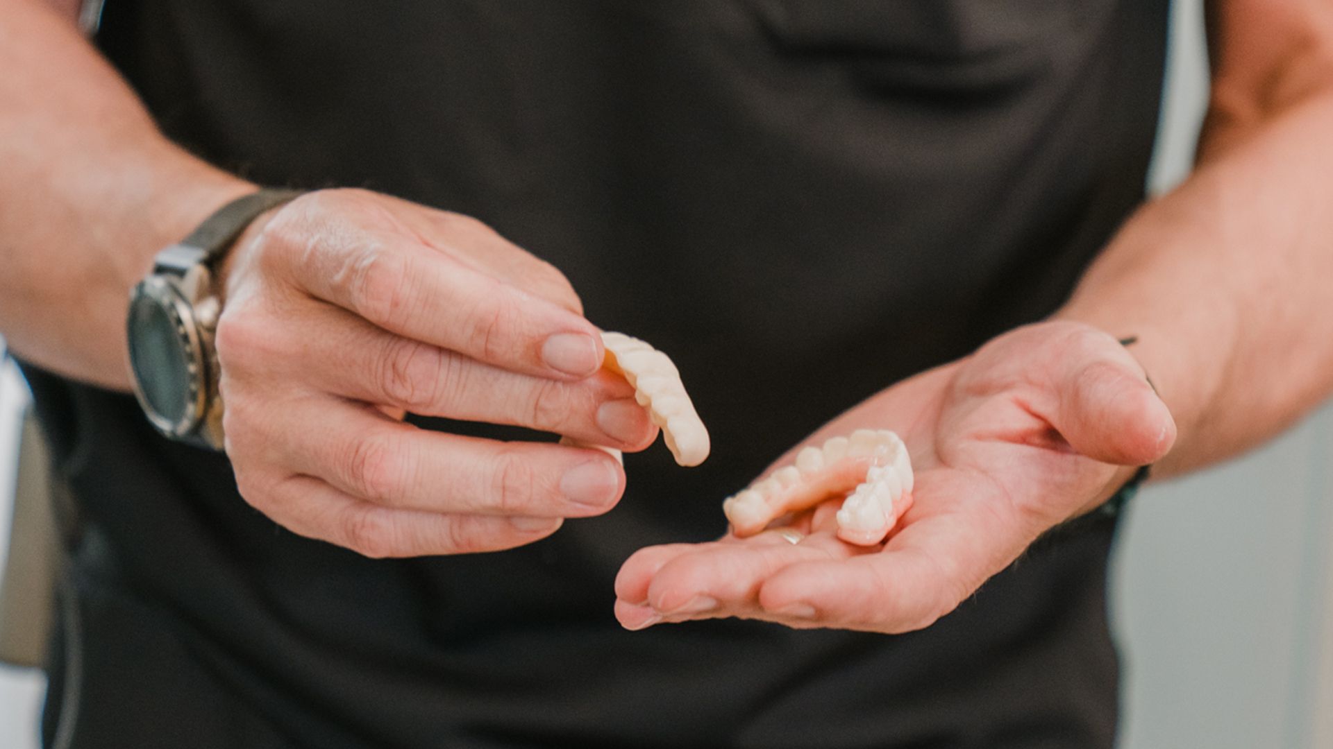 Male dental professional demonstrating clear orthodontic aligner trays in both hands outdoors