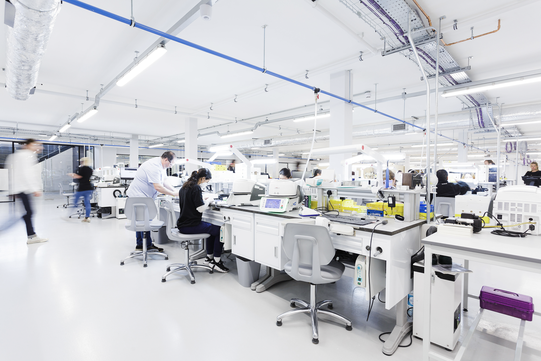 A spacious dental laboratory features multiple workstations with automated analyzers and processing equipment where technicians perform specimen analysis and dental prosthetics manufacturing.
