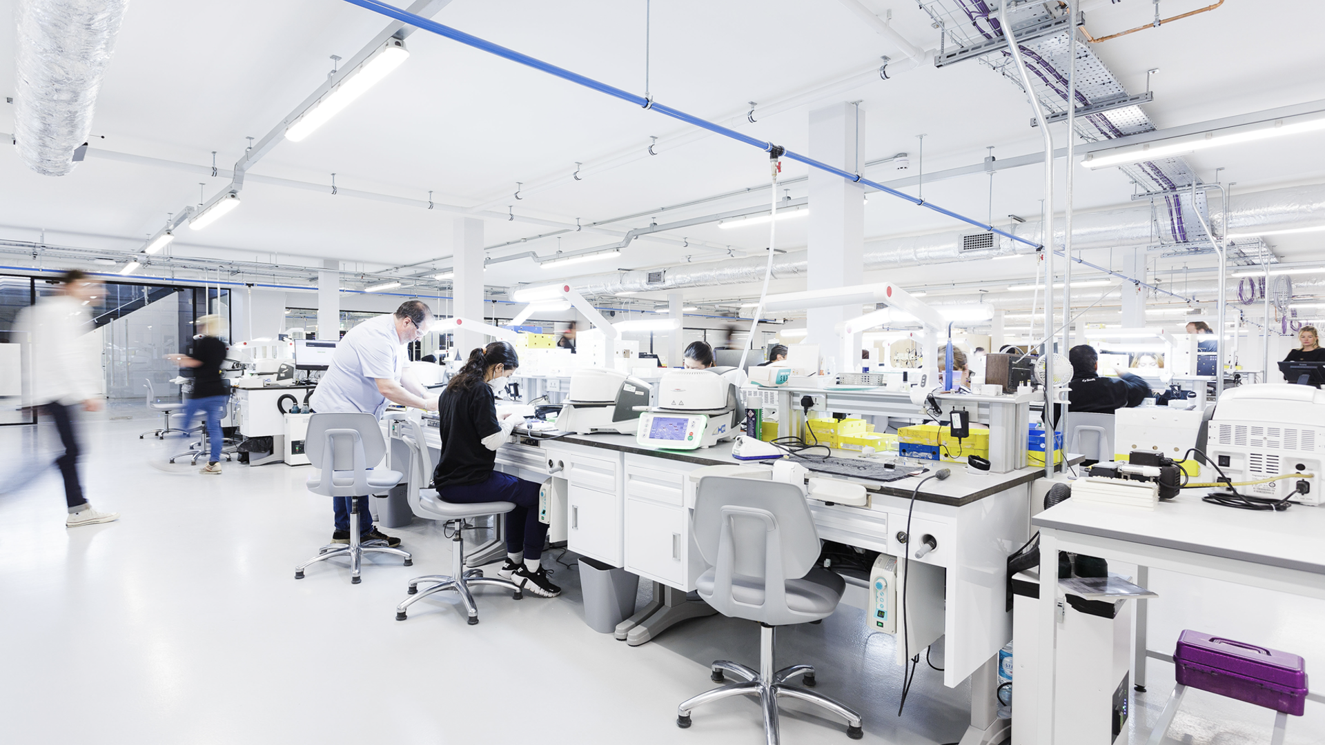 A spacious dental laboratory features multiple workstations with automated analyzers and processing equipment where technicians perform specimen analysis and dental prosthetics manufacturing.
