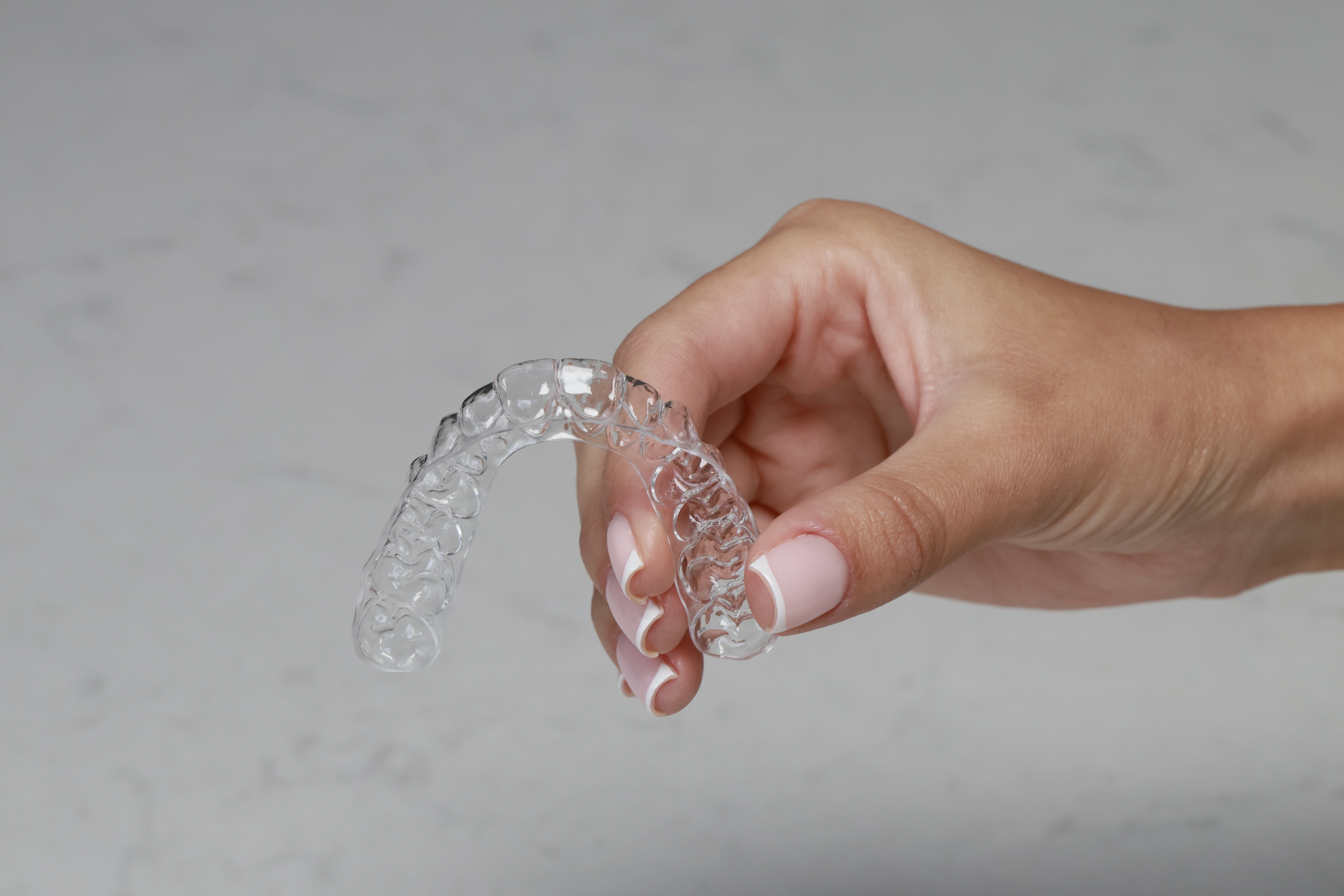 A hand holding a transparent clear aligner tray showing the detailed internal structure and tooth-tracking design used in orthodontic treatment.